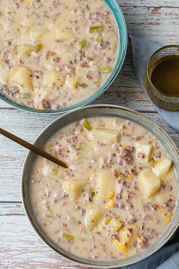 Hearty hamburger and potato soup in bowls with fresh ingredients and broth.