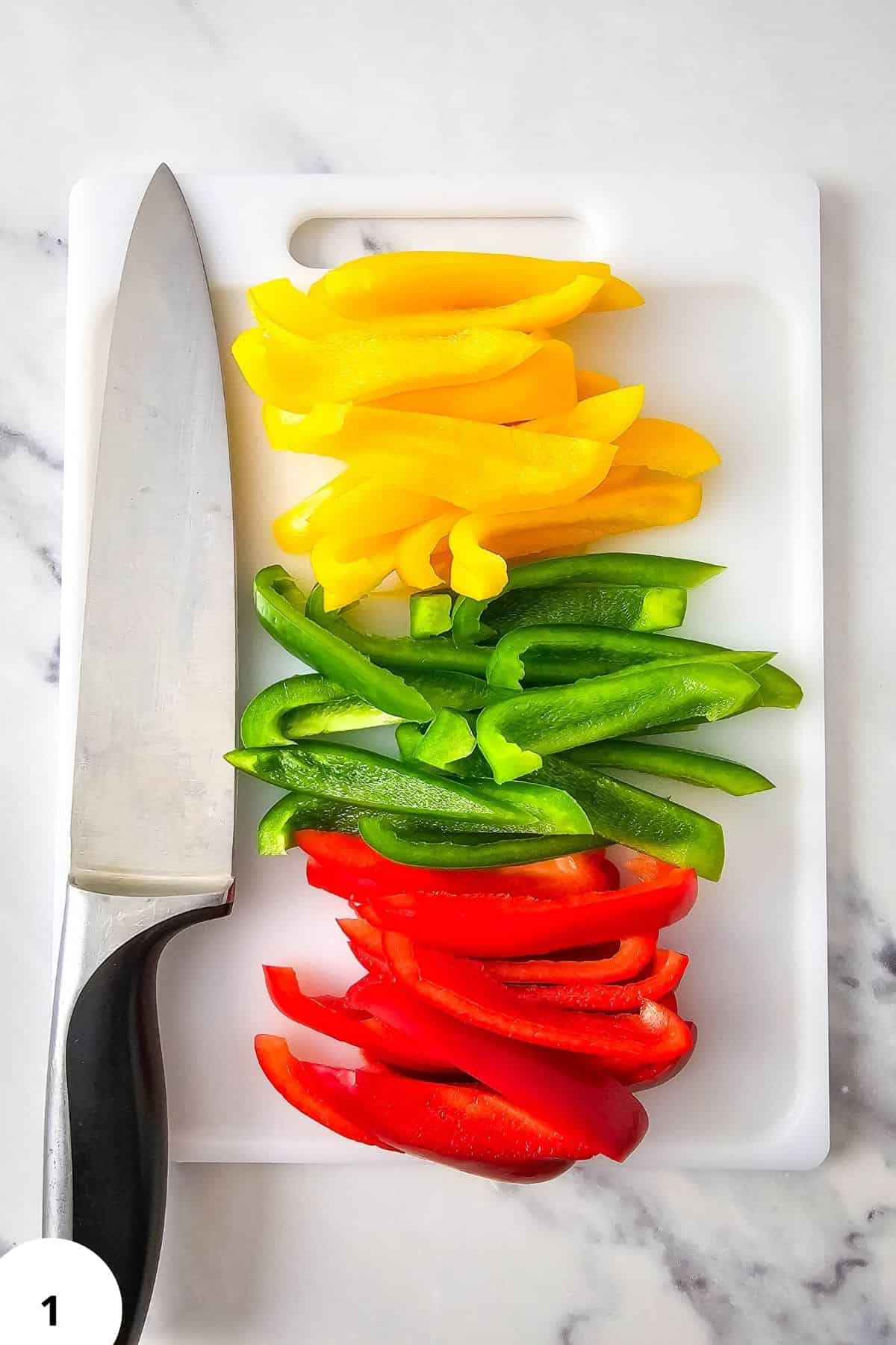 Fresh sliced yellow, green, and red bell peppers for fajitas on a white cutting board.