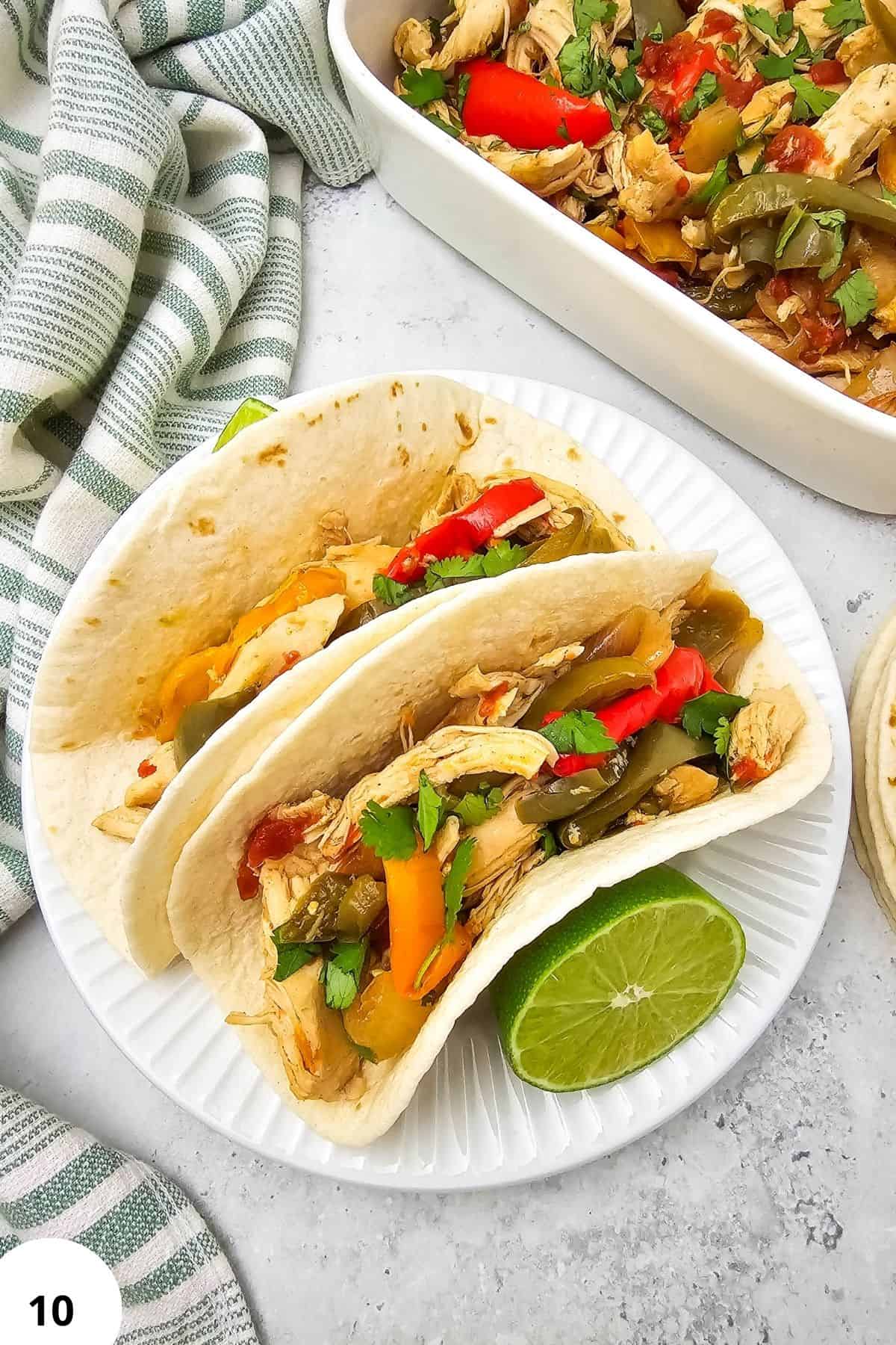 Chicken fajitas in soft tortillas with colorful peppers and lime wedge.