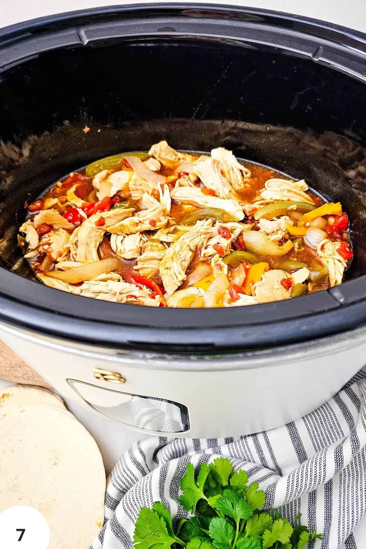 Slow cooker chicken fajitas with peppers and onions in a black slow cooker.