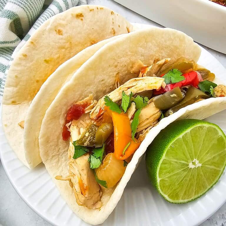 Chicken fajitas in soft tortillas with vegetables and lime wedge.