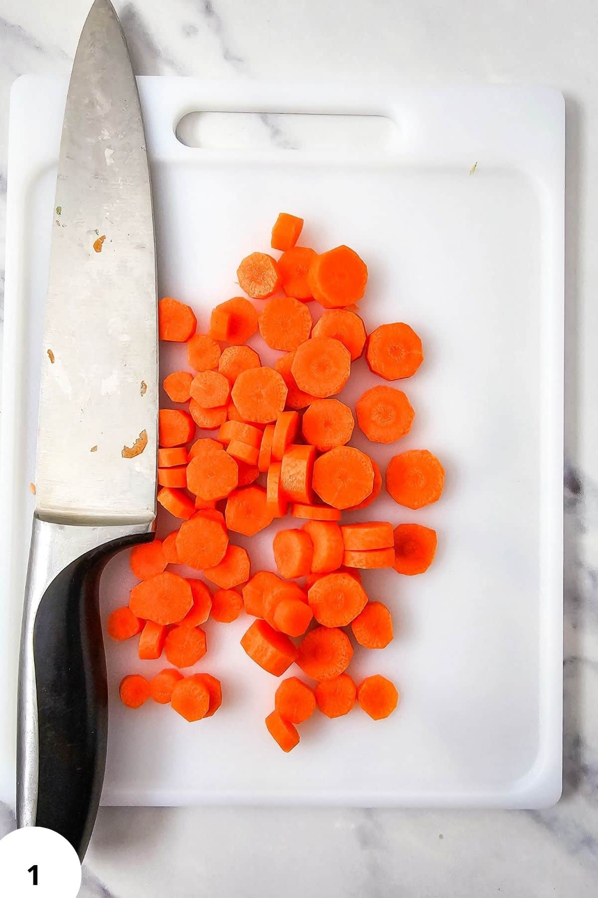 Freshly sliced carrots on a white cutting board with a knife, ready for cooking.