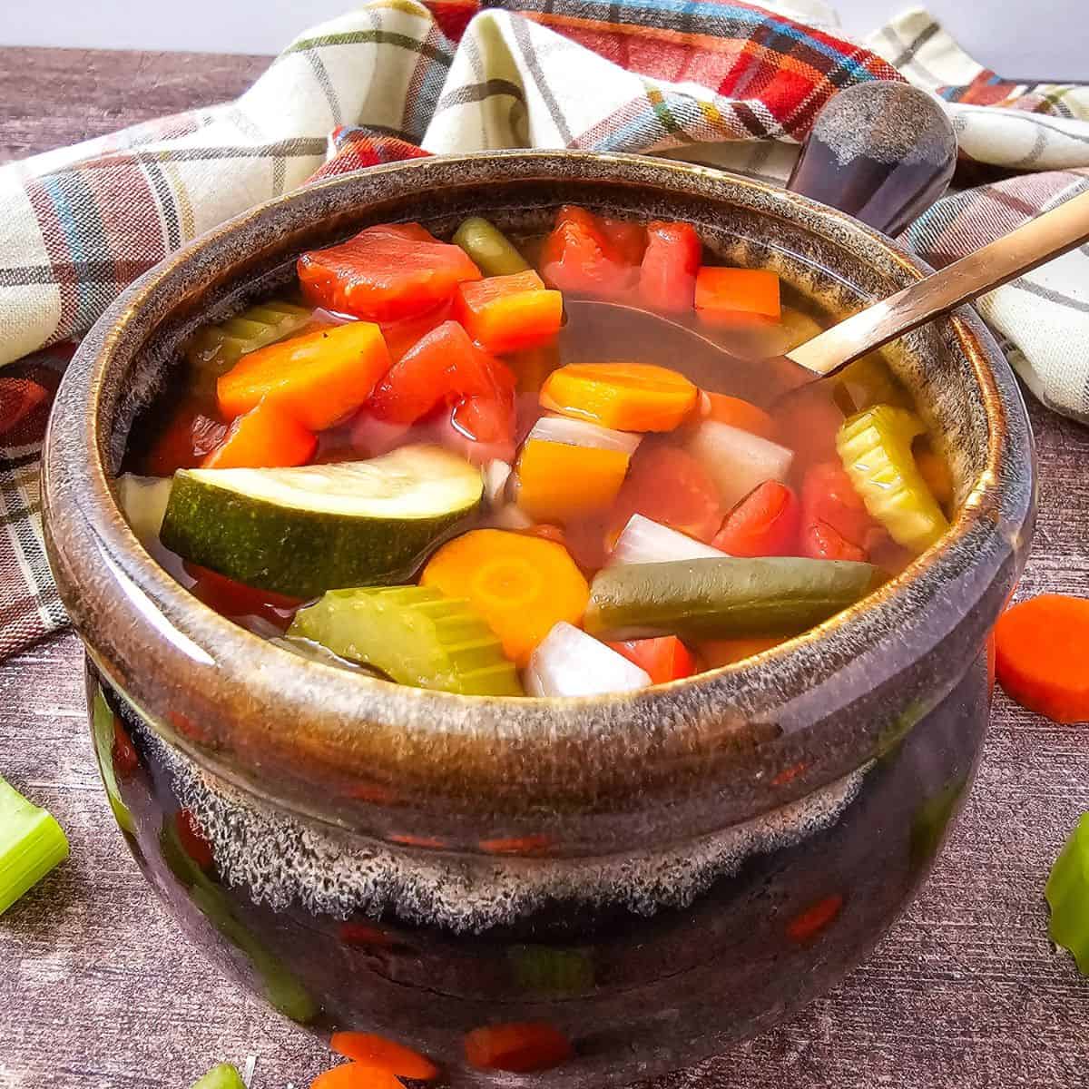 Healthy vegetable soup with fresh carrots, zucchini, and tomatoes in a clay pot.