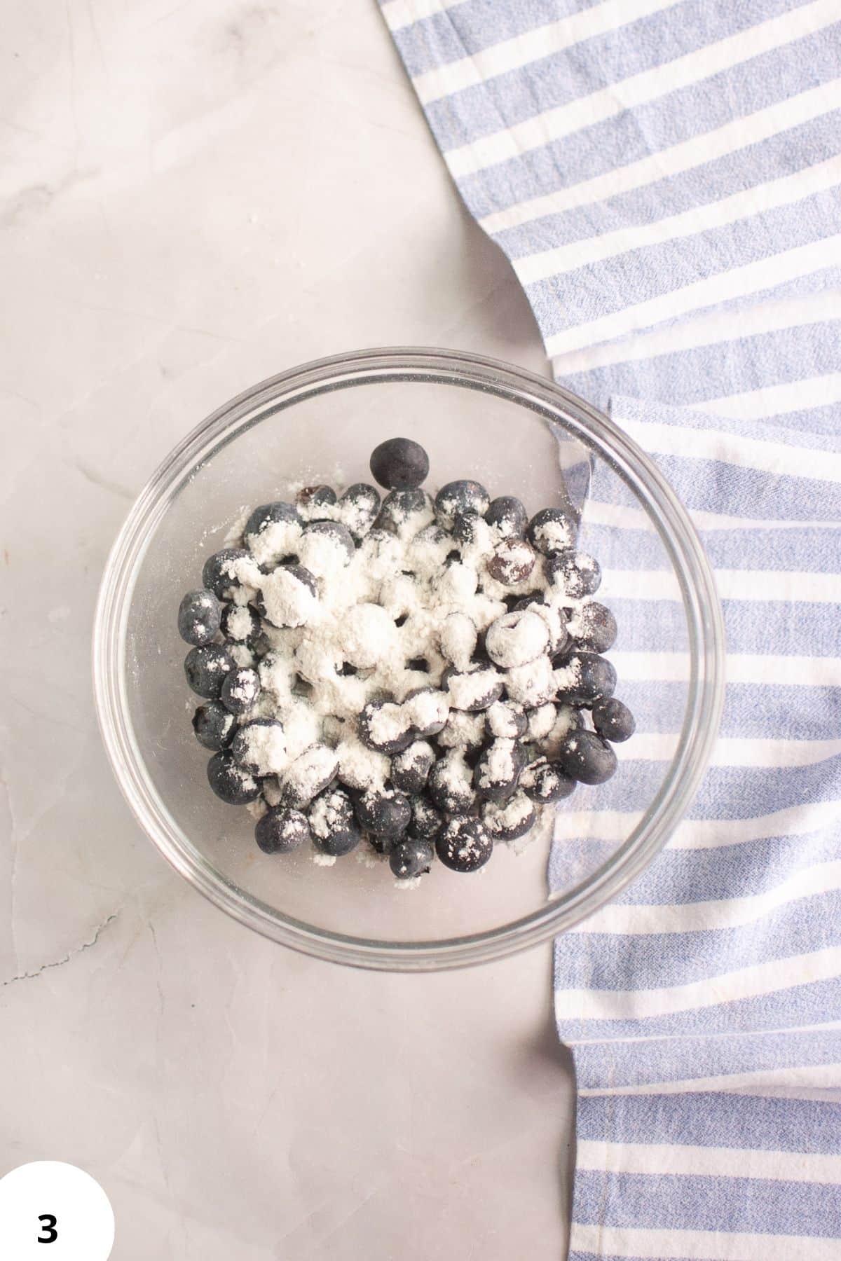 Blueberries coated with flour in a glass bowl, ready for sourdough blueberry cream scones.
