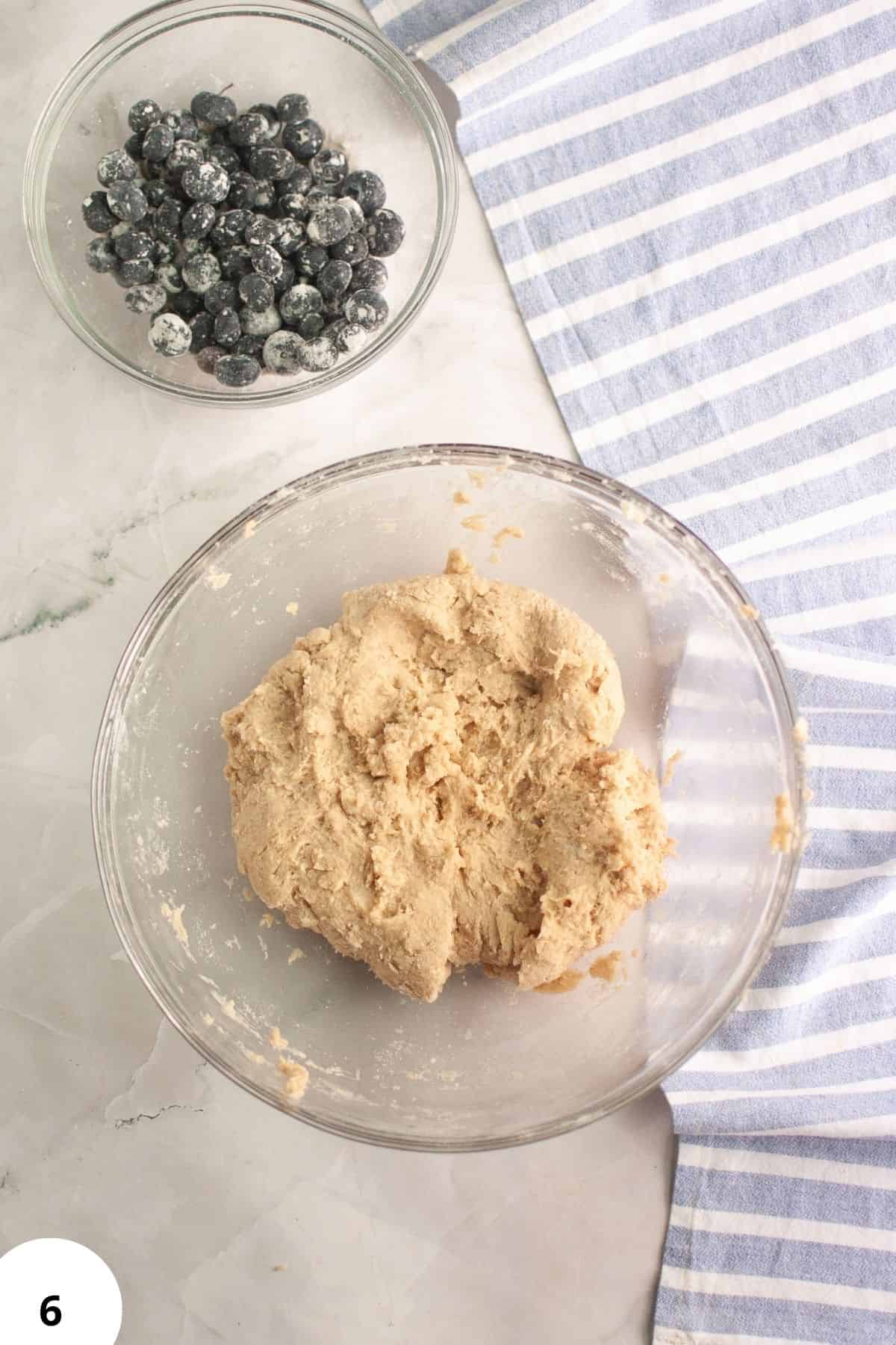 Sourdough blueberry scones dough being prepared with blueberries in a glass bowl.