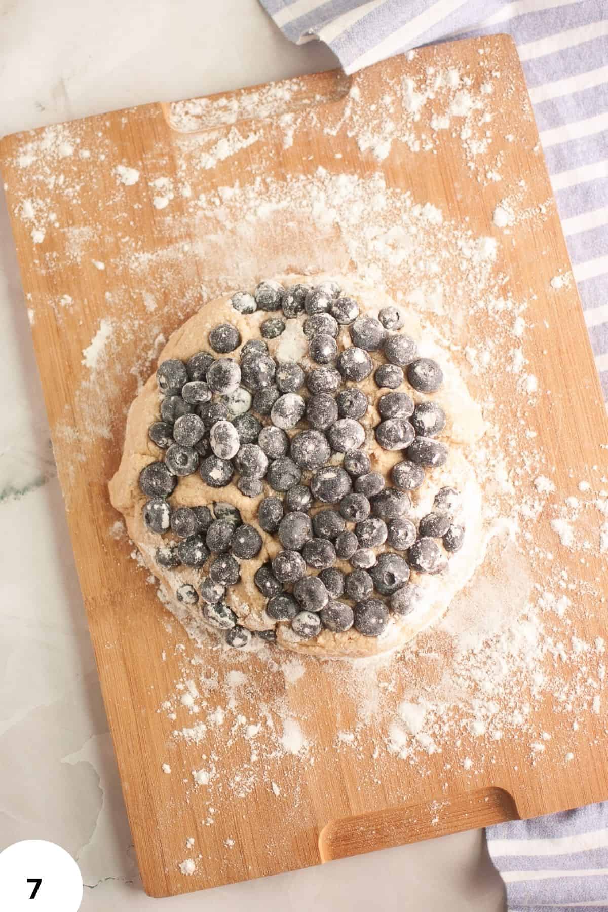 Freshly prepared sourdough blueberry cream scone on floured wooden board.