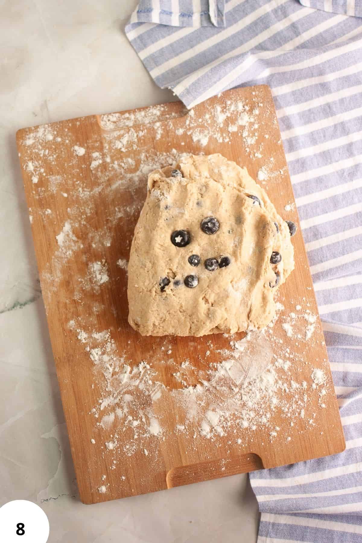 Sourdough blueberry scone dough with blueberries on a floured wooden board.