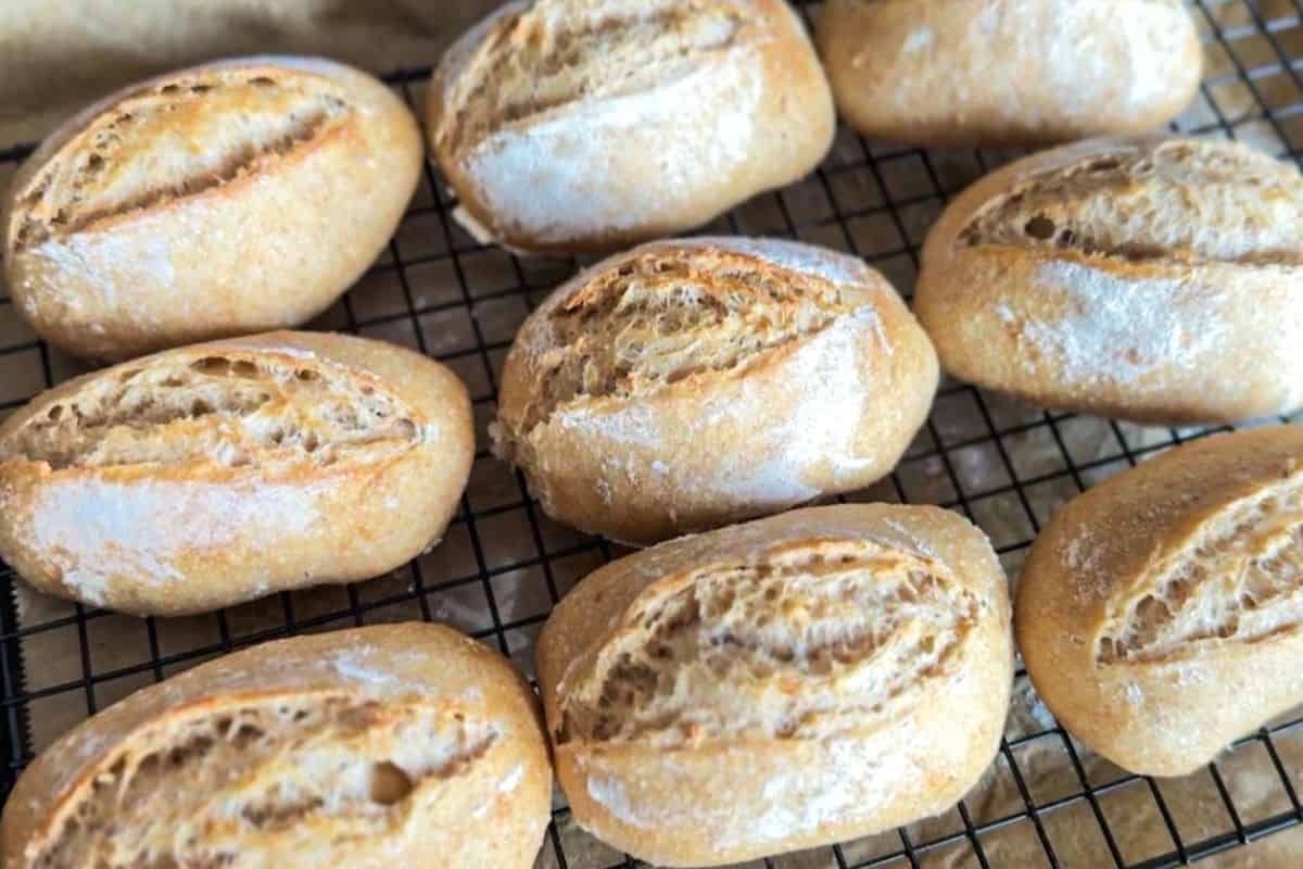Golden bread rolls cooling on a wire rack, perfect for sourdough bread lovers.