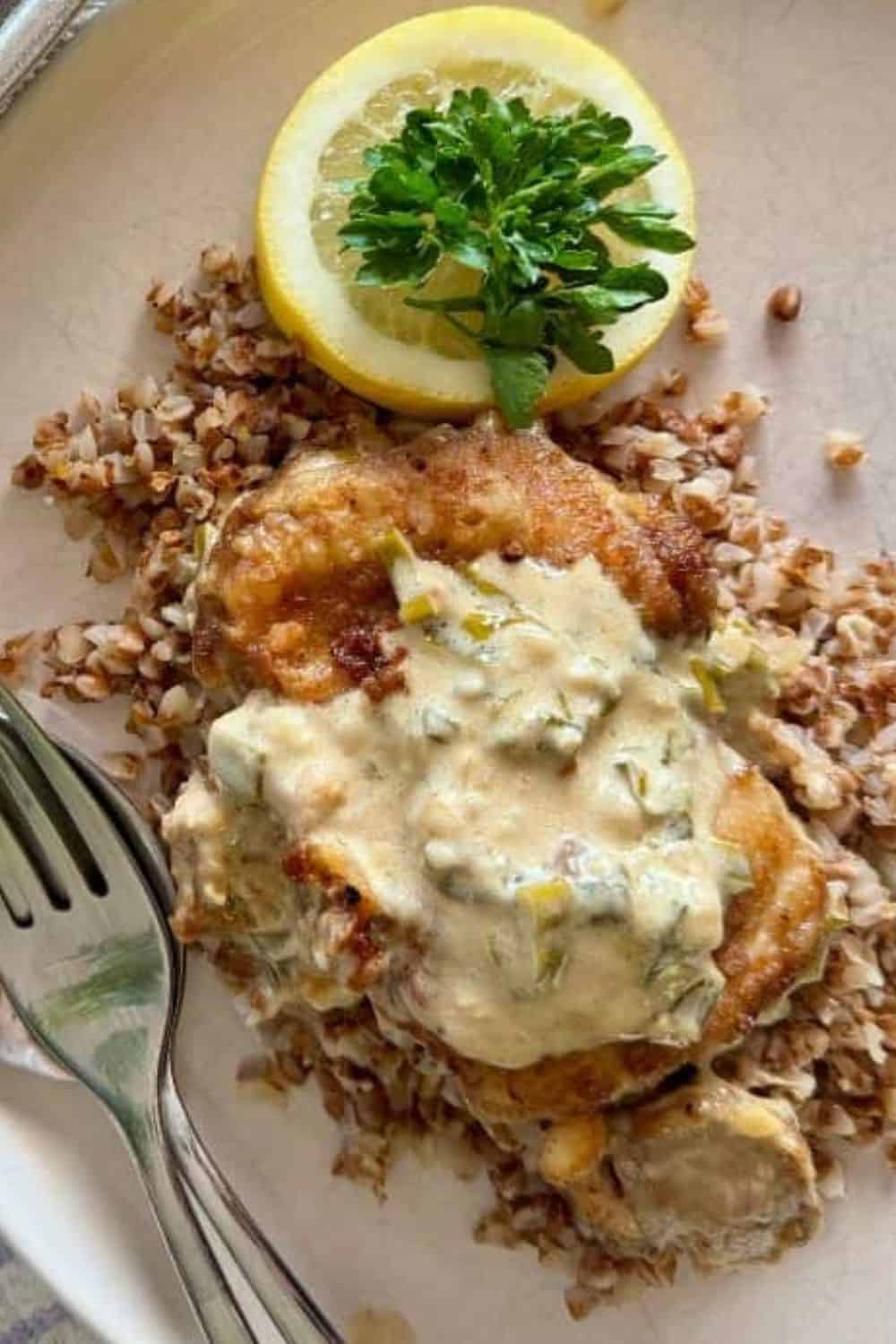 Baked fish topped with creamy herb sauce, served with lemon slices and fresh parsley. Perfect for he.