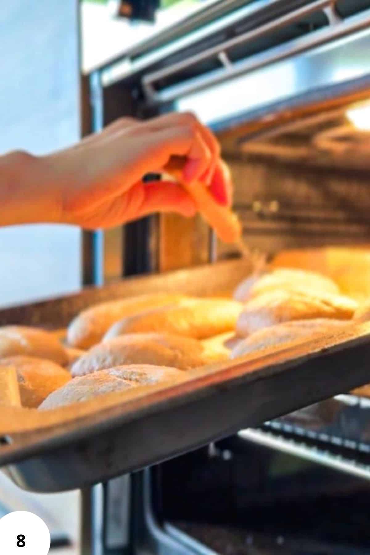 Hand placing sourdough spelt rolls in oven for baking.