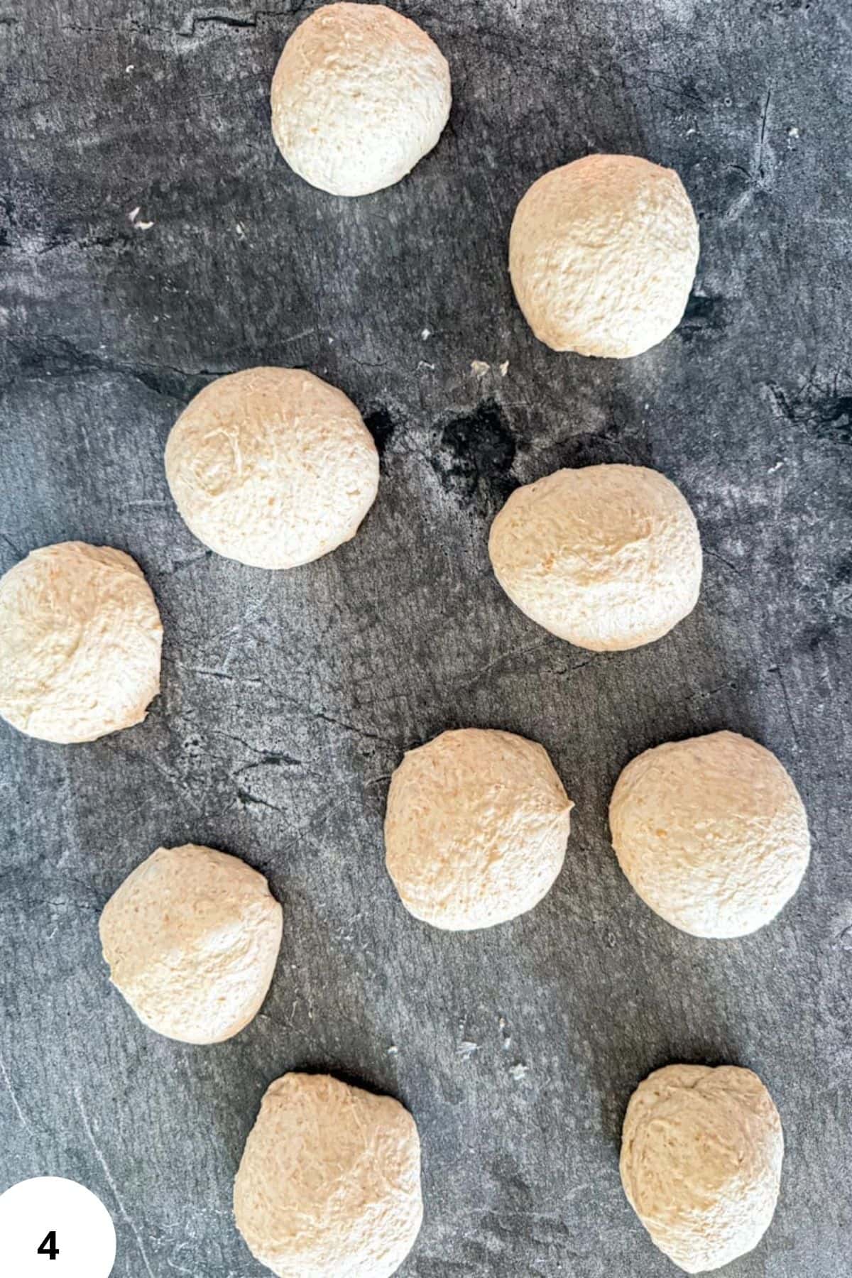 Fresh sourdough spelt rolls ready for baking on a dark surface.