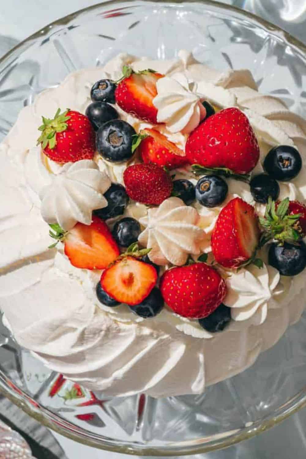 Delicious berry dessert featuring strawberries, blueberries, and whipped cream in a glass bowl.