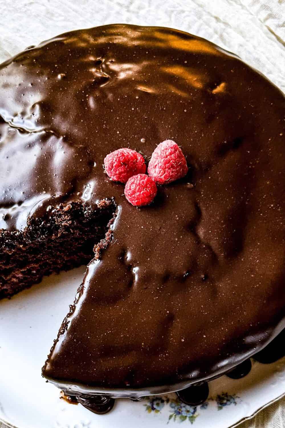 Chocolate cake with glossy chocolate glaze and fresh raspberries on top.