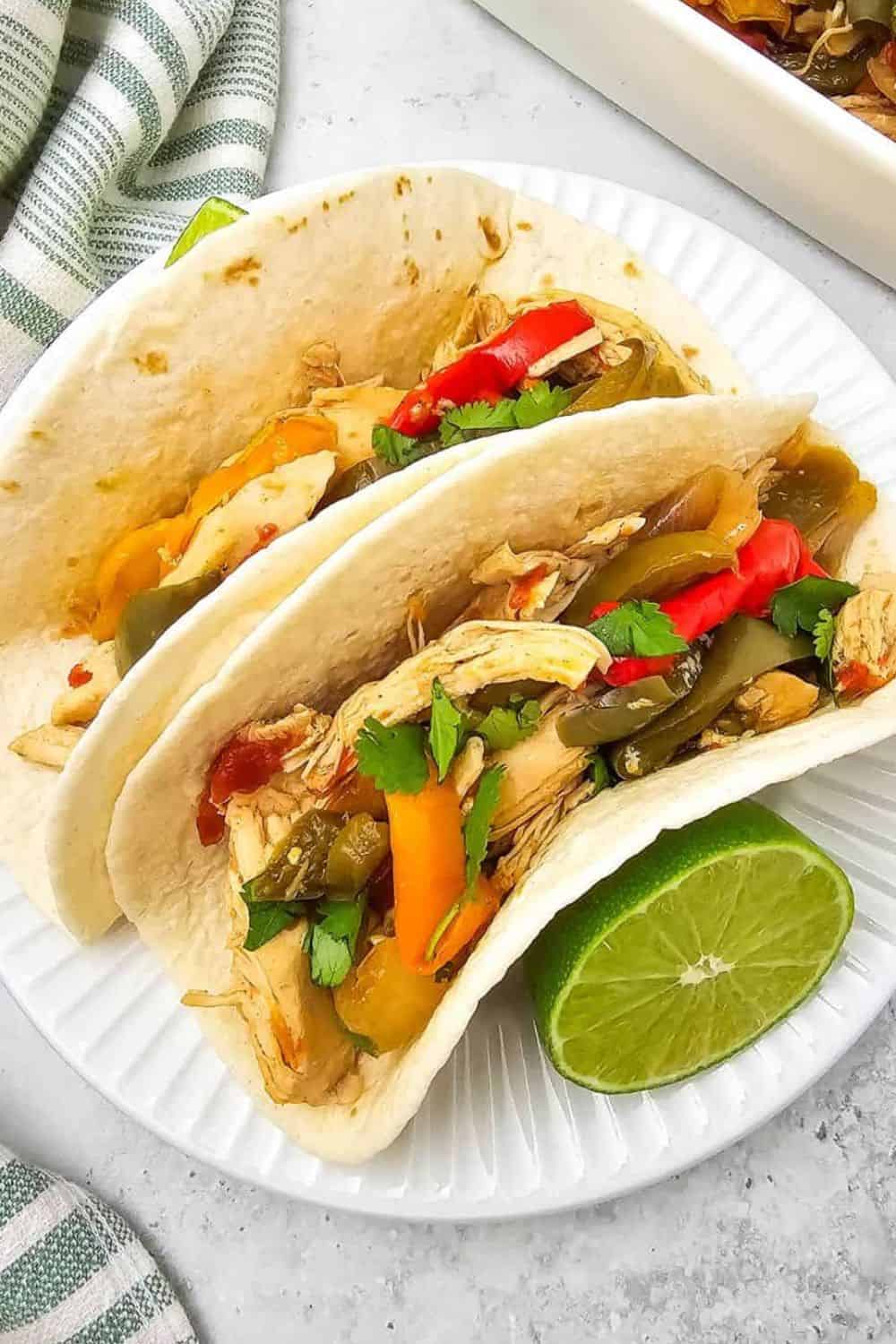 Fresh vegetable tacos with colorful peppers, cilantro, and lime wedge on a white plate.