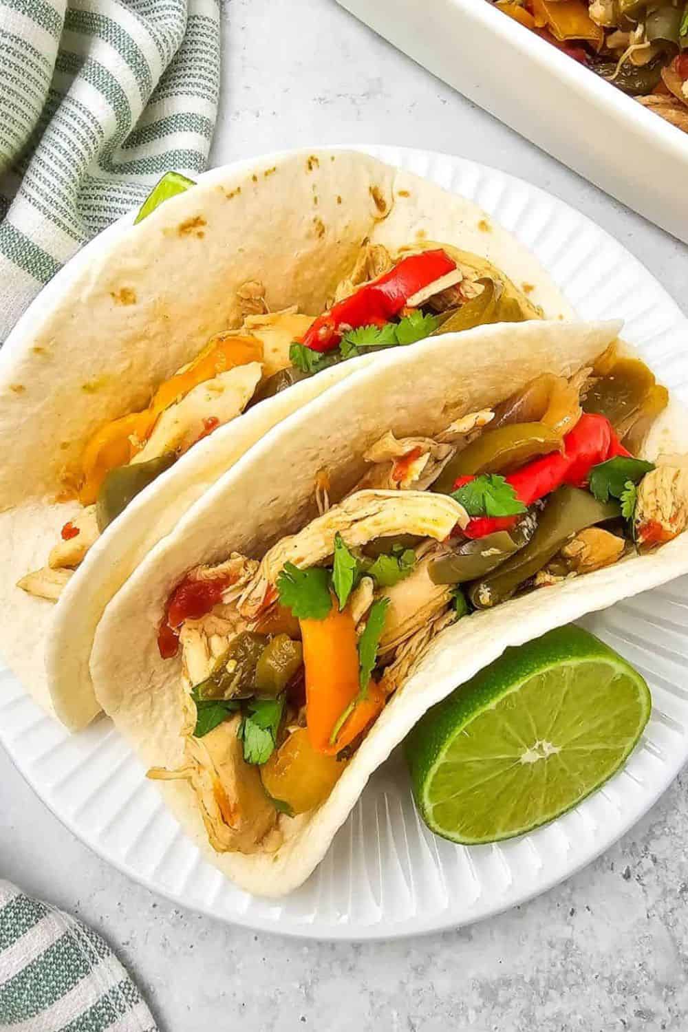 Chicken tacos with peppers, cilantro, and lime on a white plate.