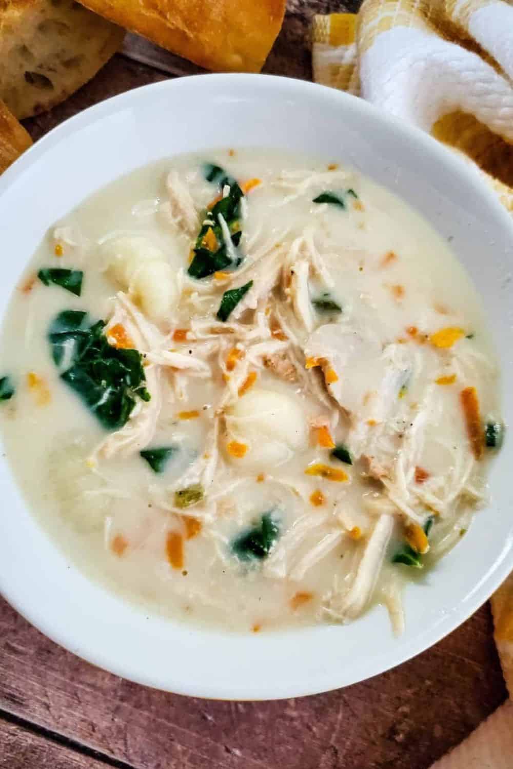 Creamy chicken and vegetable soup with shredded chicken, spinach, and carrots in a white bowl.
