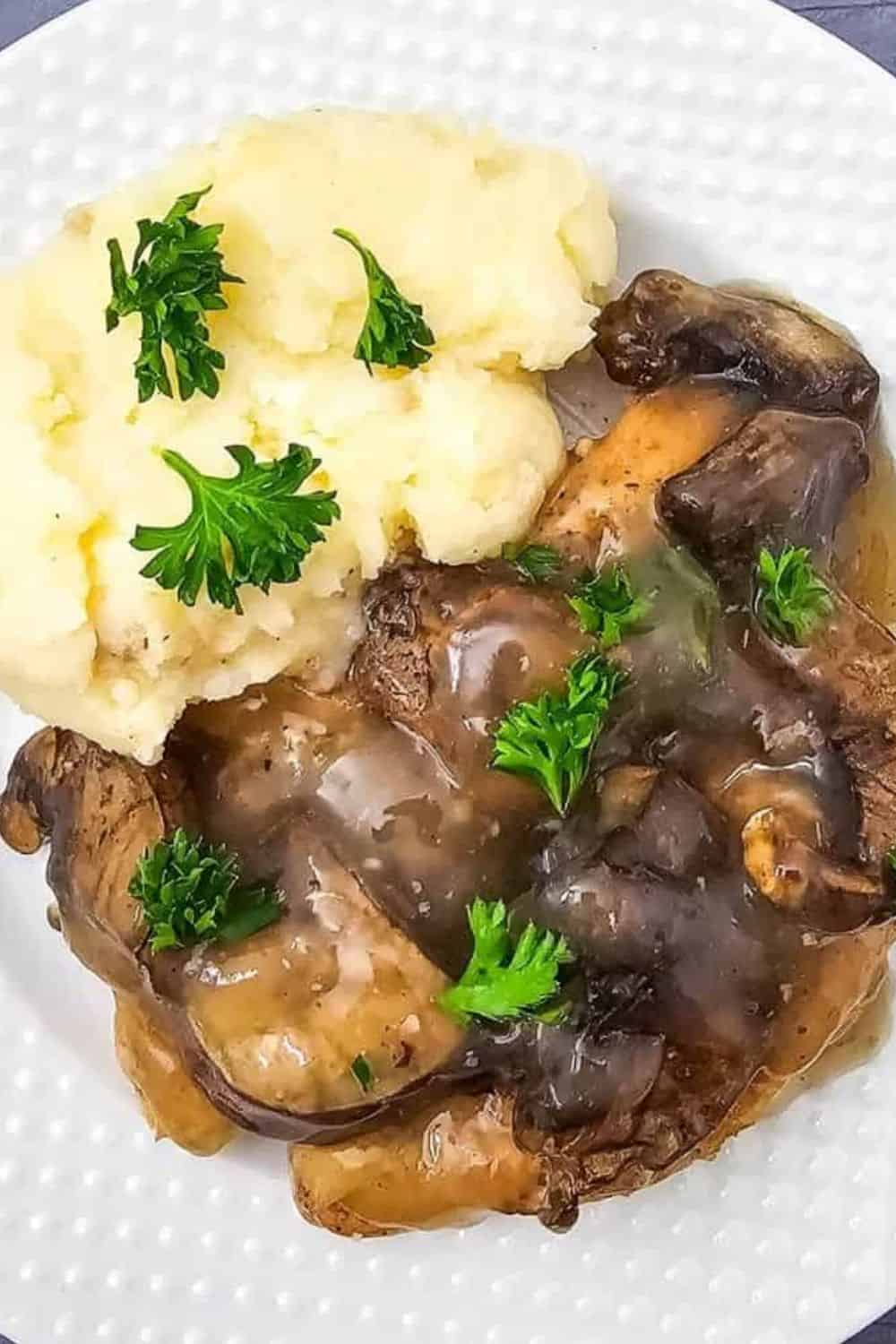 Mashed potatoes with mushroom gravy garnished with parsley on a white plate.