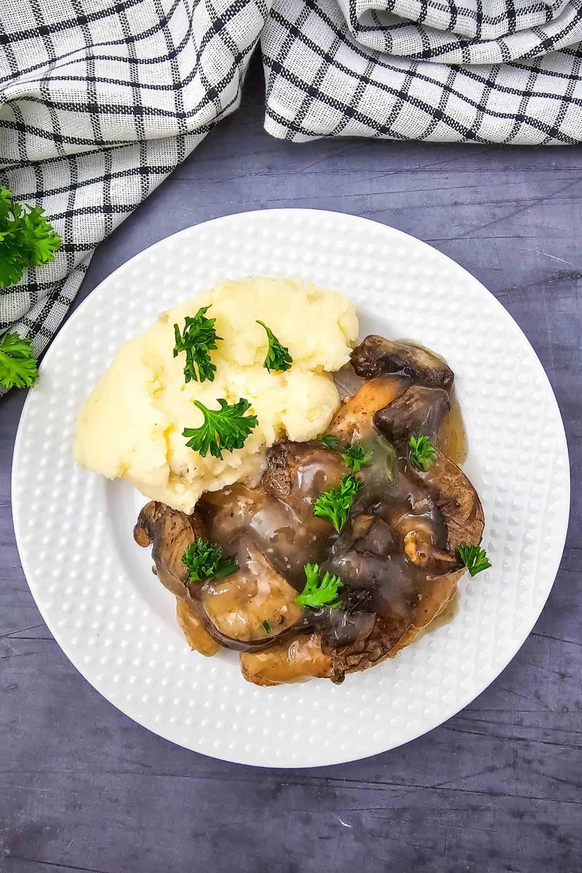 Chicken Marsala with mashed potatoes and herbs on a white plate.