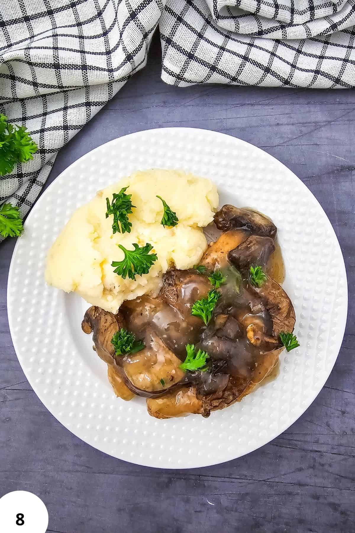 Chicken Marsala with mashed potatoes and herbs on a white plate.