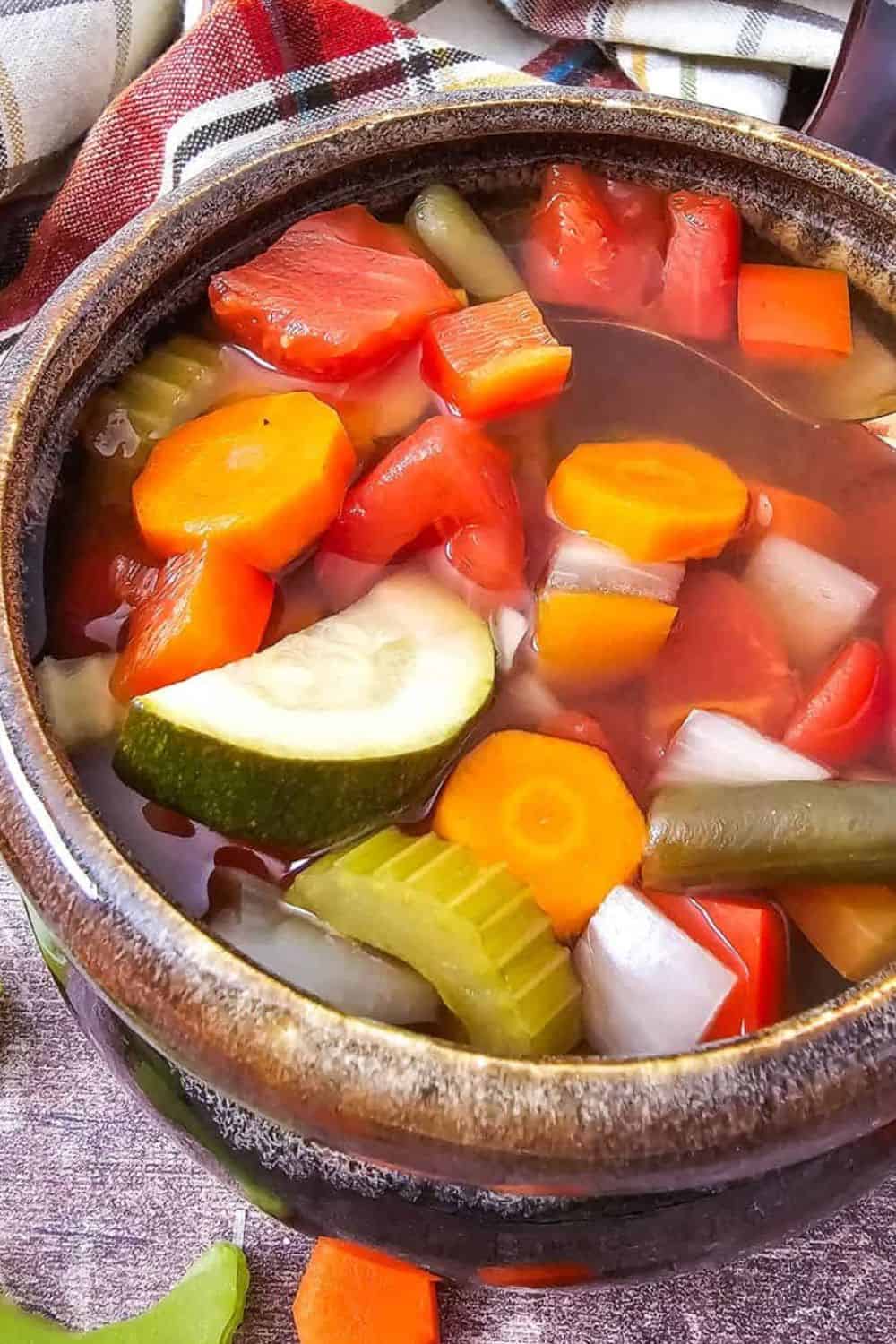 Vegetable soup with tomatoes, carrots, celery, and zucchini in a rustic bowl.