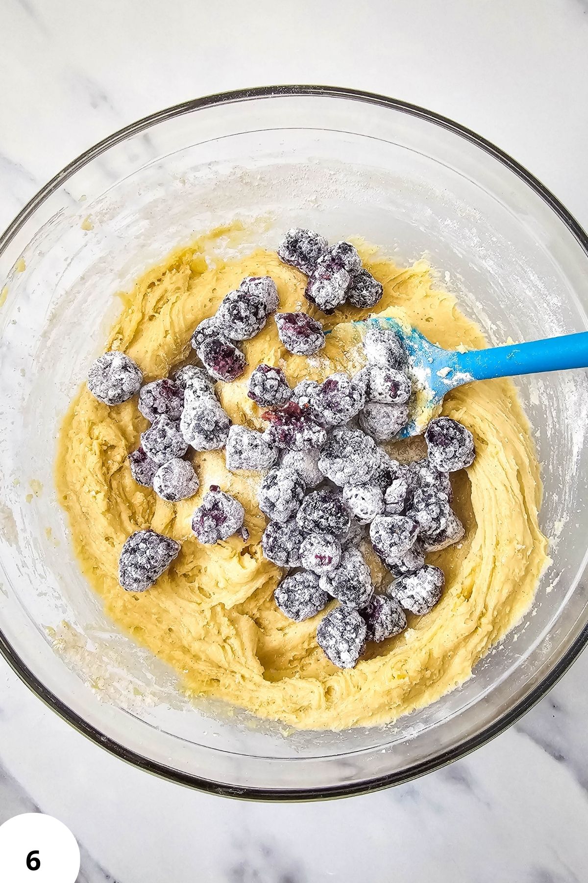 Blackberry muffin batter with frozen berries in a glass bowl for baking.