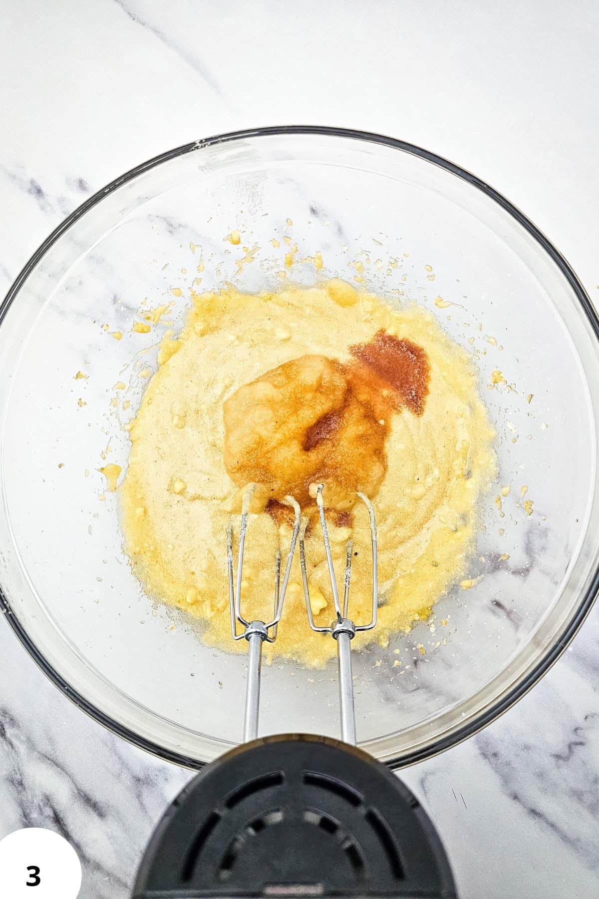 Mixing cookie dough with applesauce and raisins in a glass bowl.