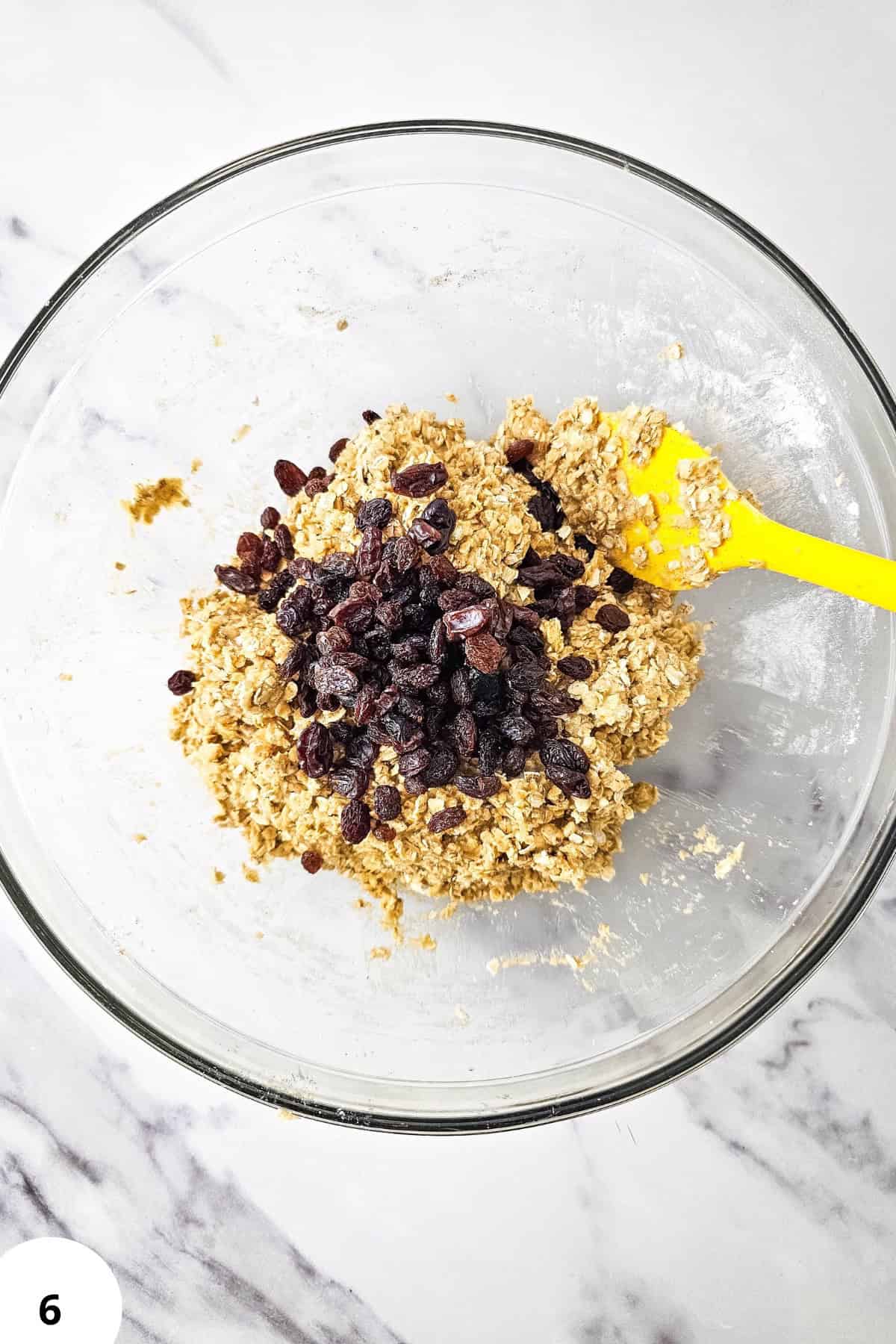 Oatmeal raisin cookie dough with raisins in a glass mixing bowl.