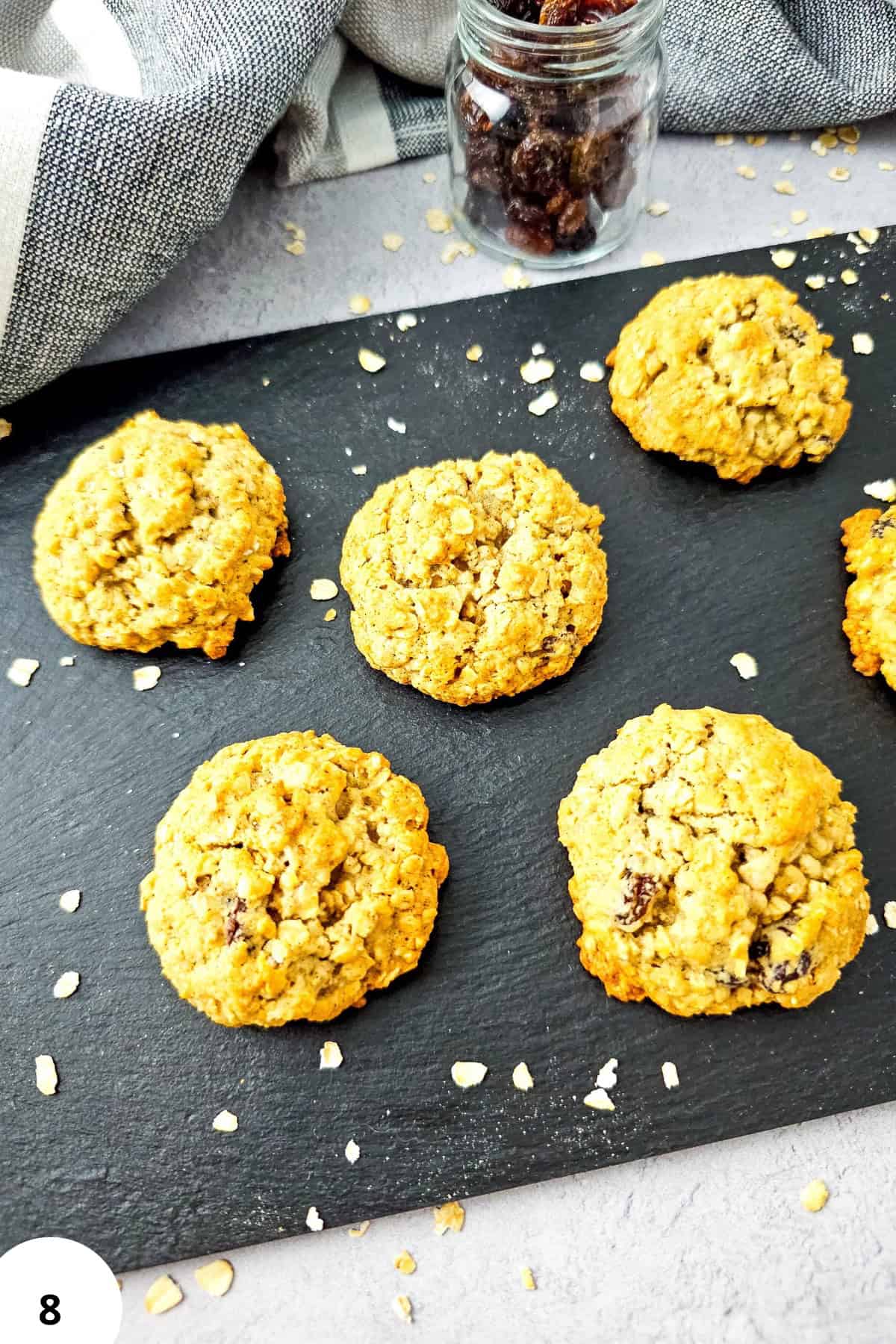 Freshly baked oatmeal raisin cookies on a black slate serving board.