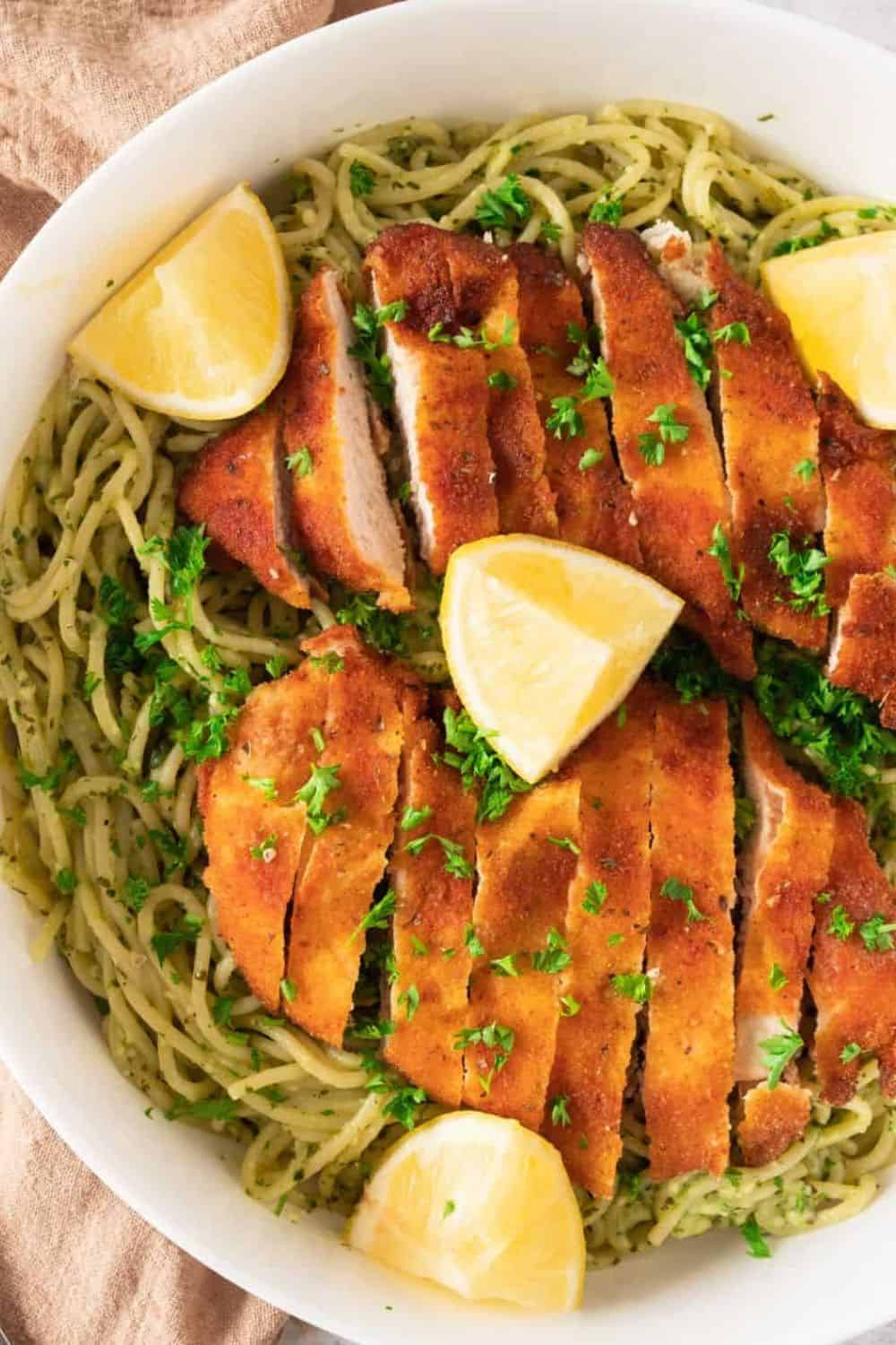 Crispy breaded chicken served over spaghetti with lemon wedges and fresh herbs.