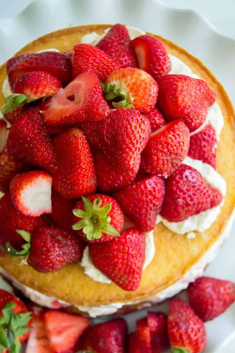 Fresh strawberries piled on a cake with cream frosting.