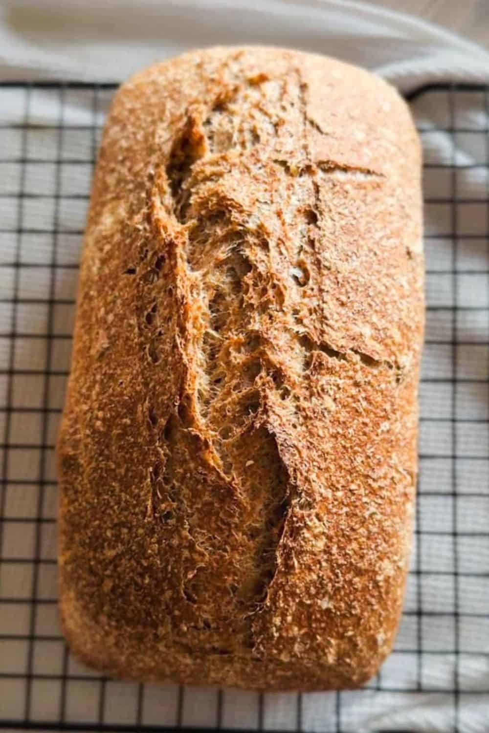 Bread loaf cooling on a wire rack, showcasing a golden crust and rustic texture.