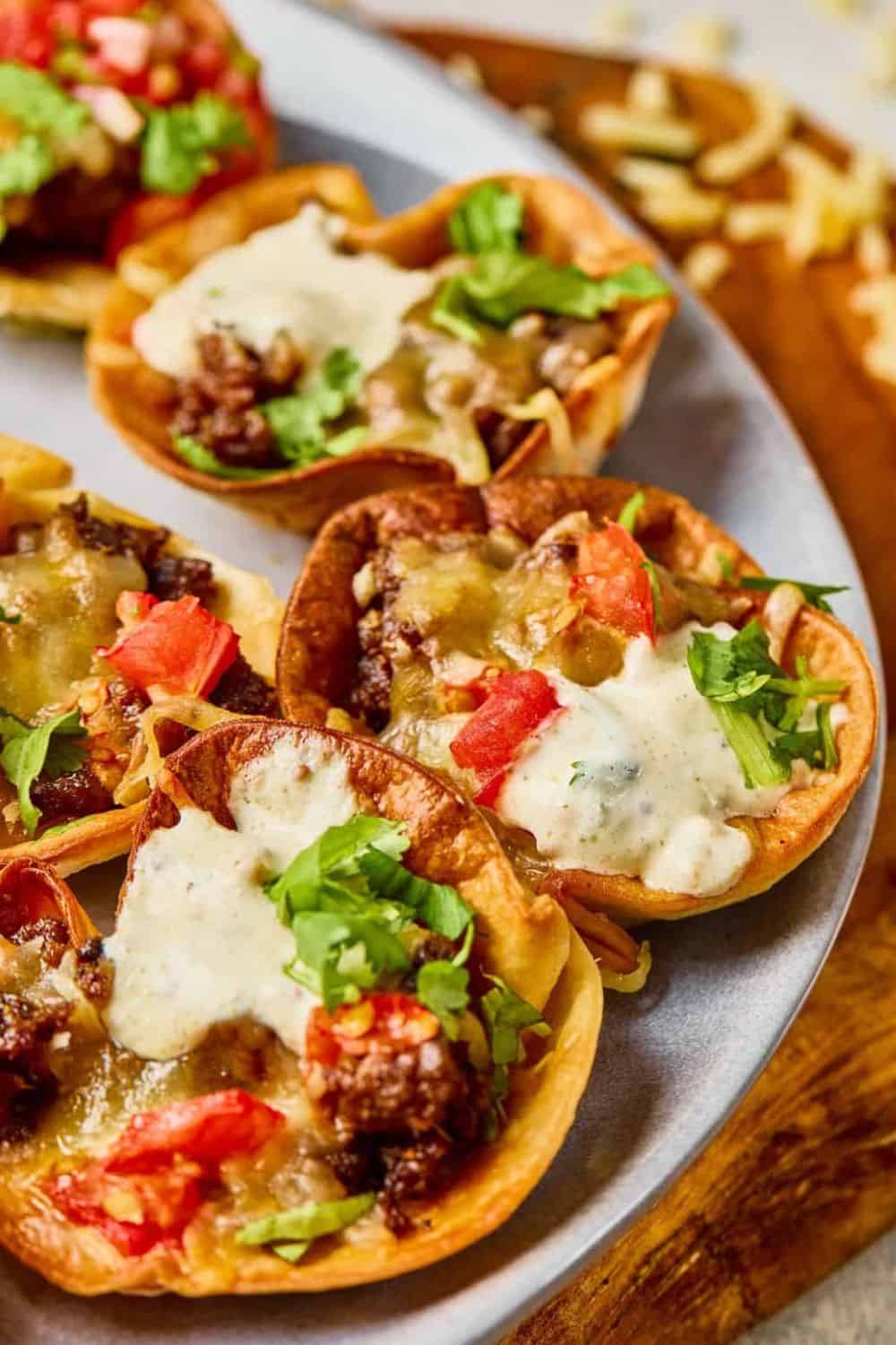 Mini ground beef tacos with cheese, tomatoes, and cilantro on a plate.
