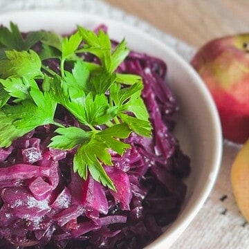 Fresh braised red cabbage with apple garnished with parsley in a white bowl.