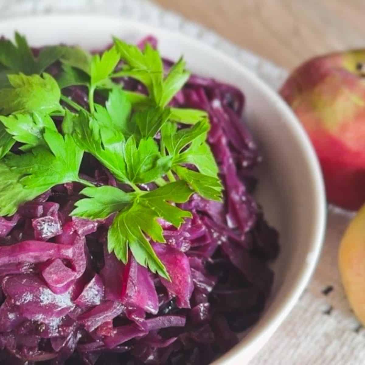 Fresh braised red cabbage with apple garnished with parsley in a white bowl.