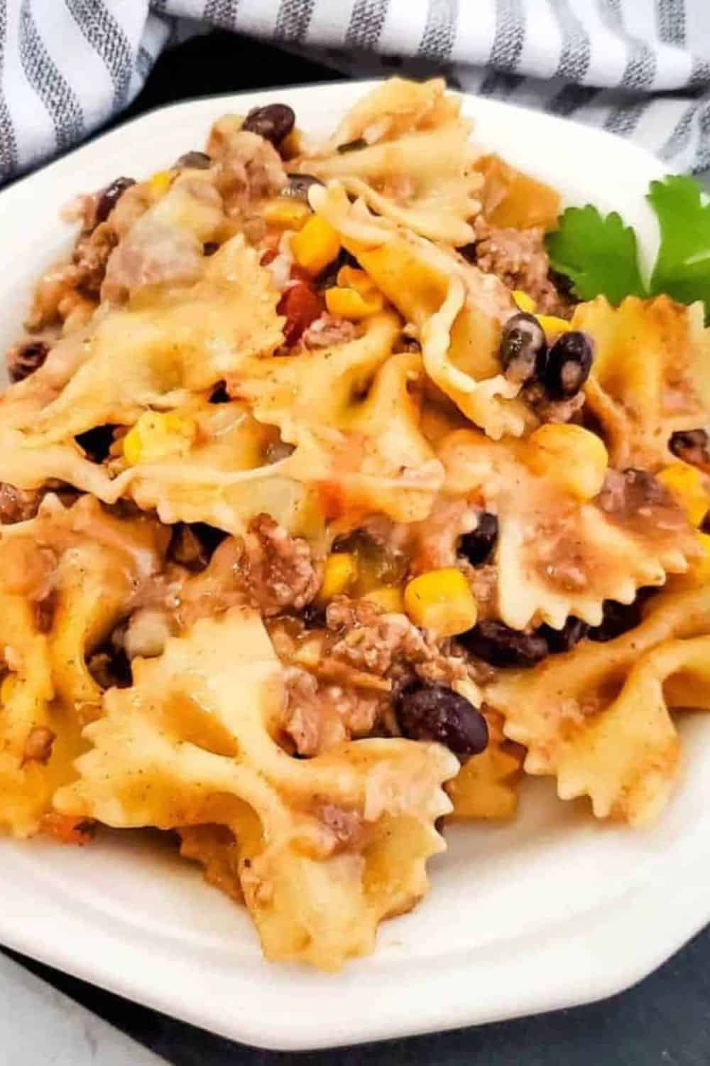 Delicious ground beef pasta bake with cheese, beans, and vegetables on a white plate.