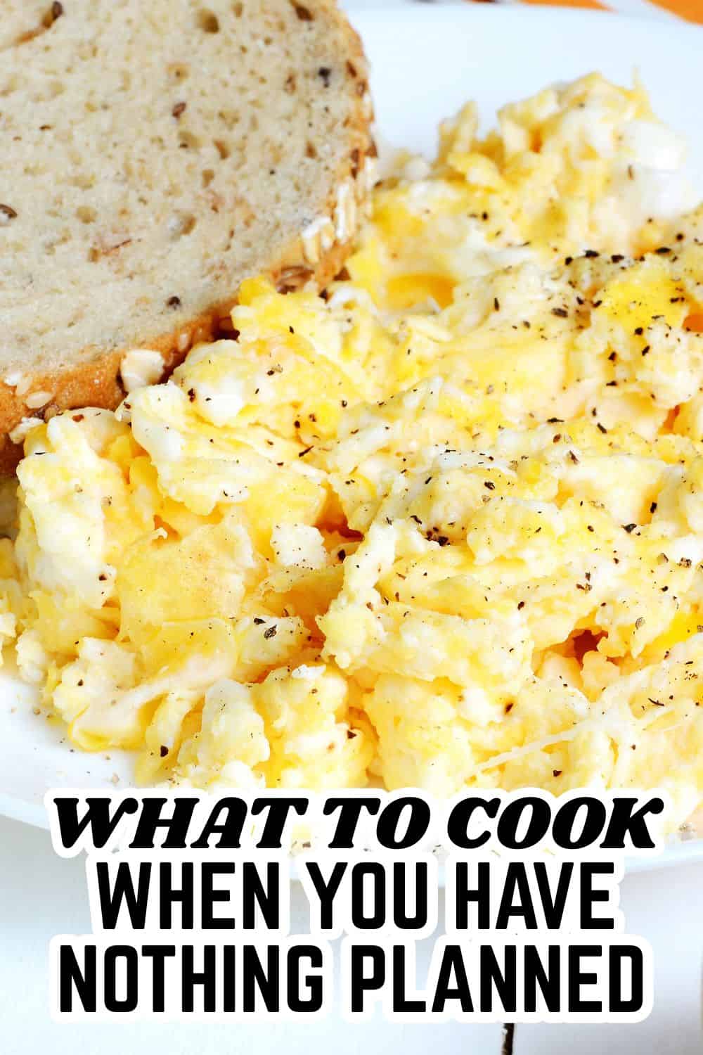 Freshly scrambled eggs with black pepper served with bread slice on white plate.