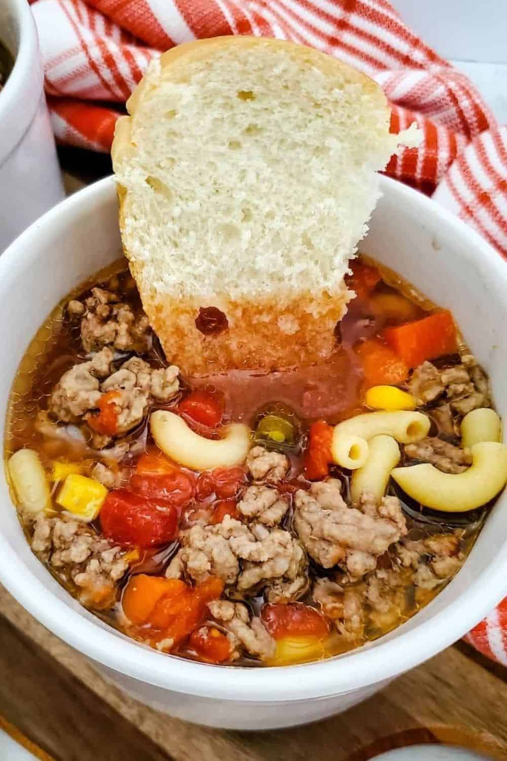 Hearty ground beef soup with vegetables and pasta, served with bread.