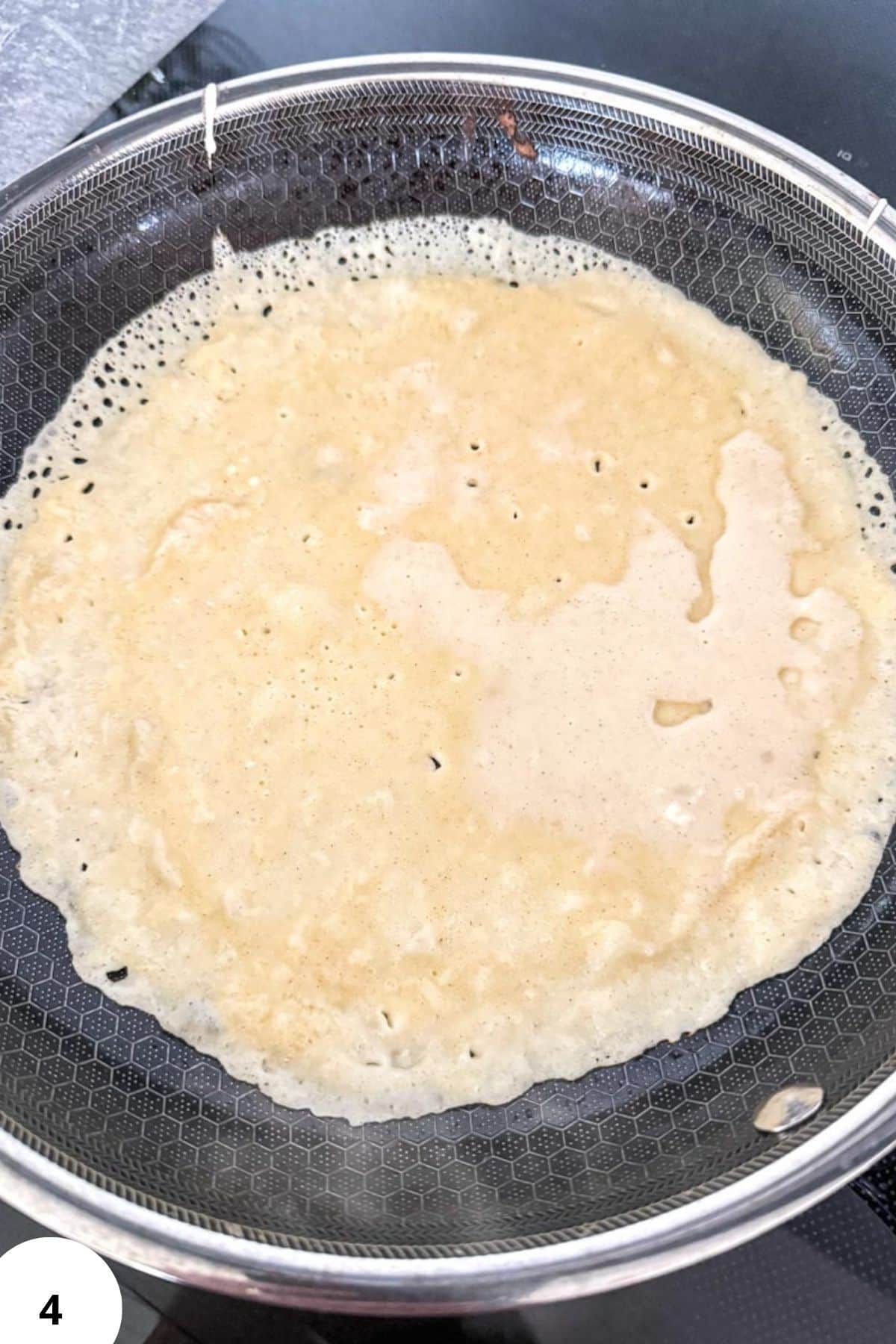 Thin sourdough crepe cooking in a non-stick pan, ready for filling.
