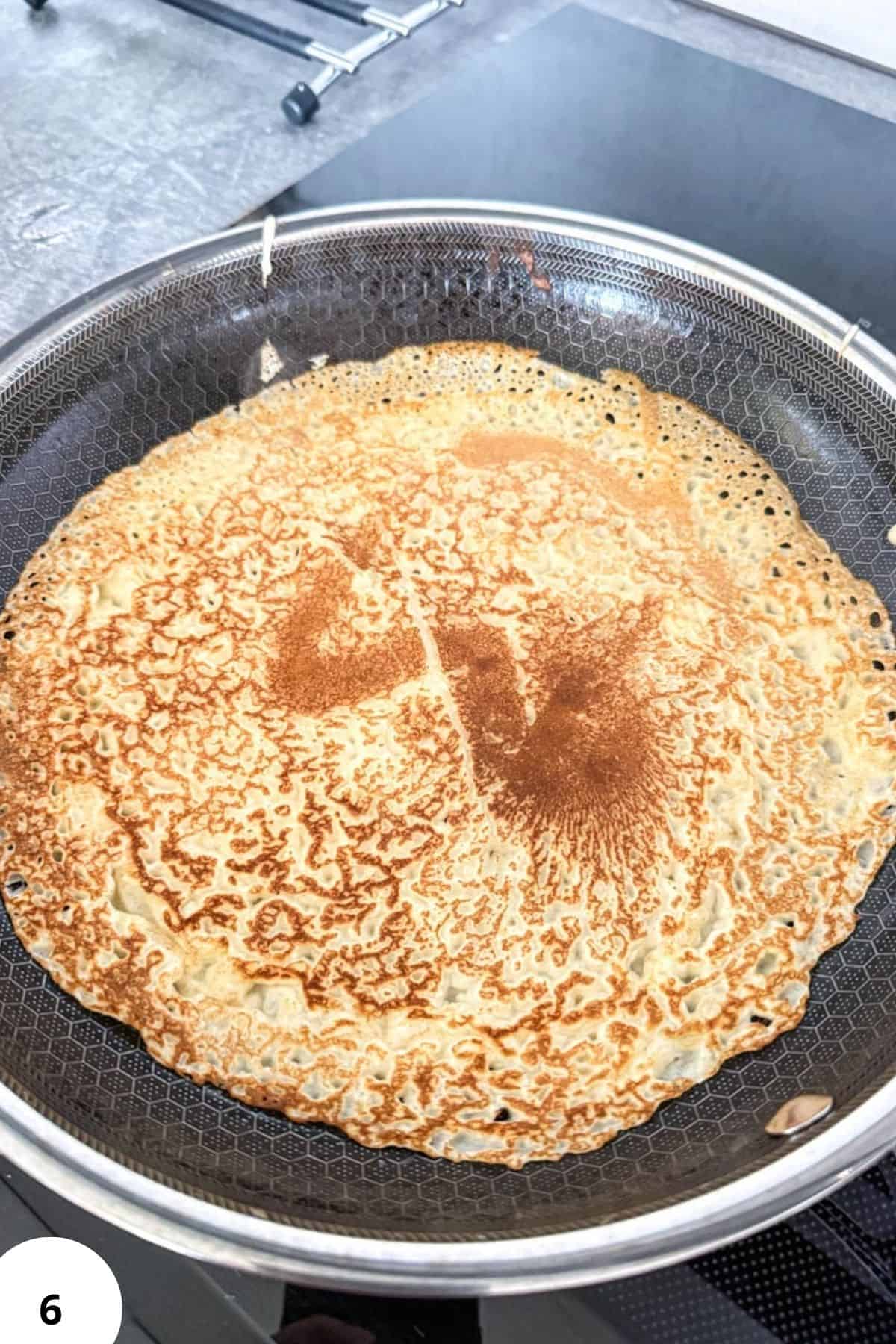 Sourdough crepe cooking on a non-stick pan, golden and crispy.