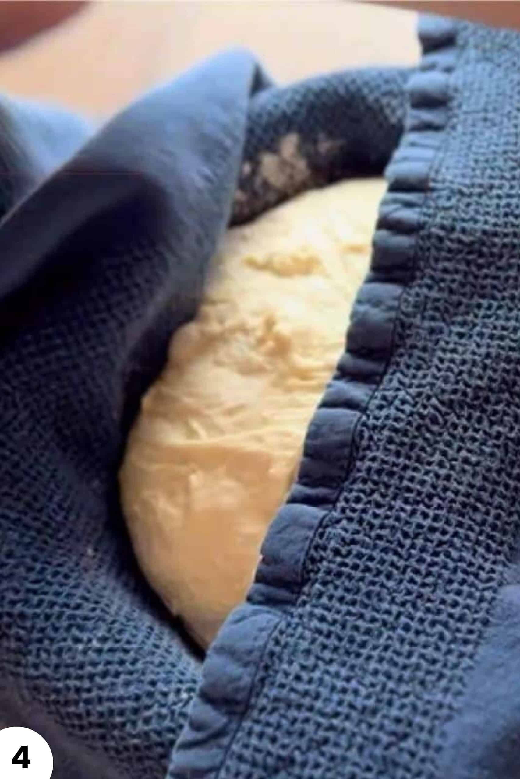 Dough being stretched and folded inside a blue cloth for bread baking.