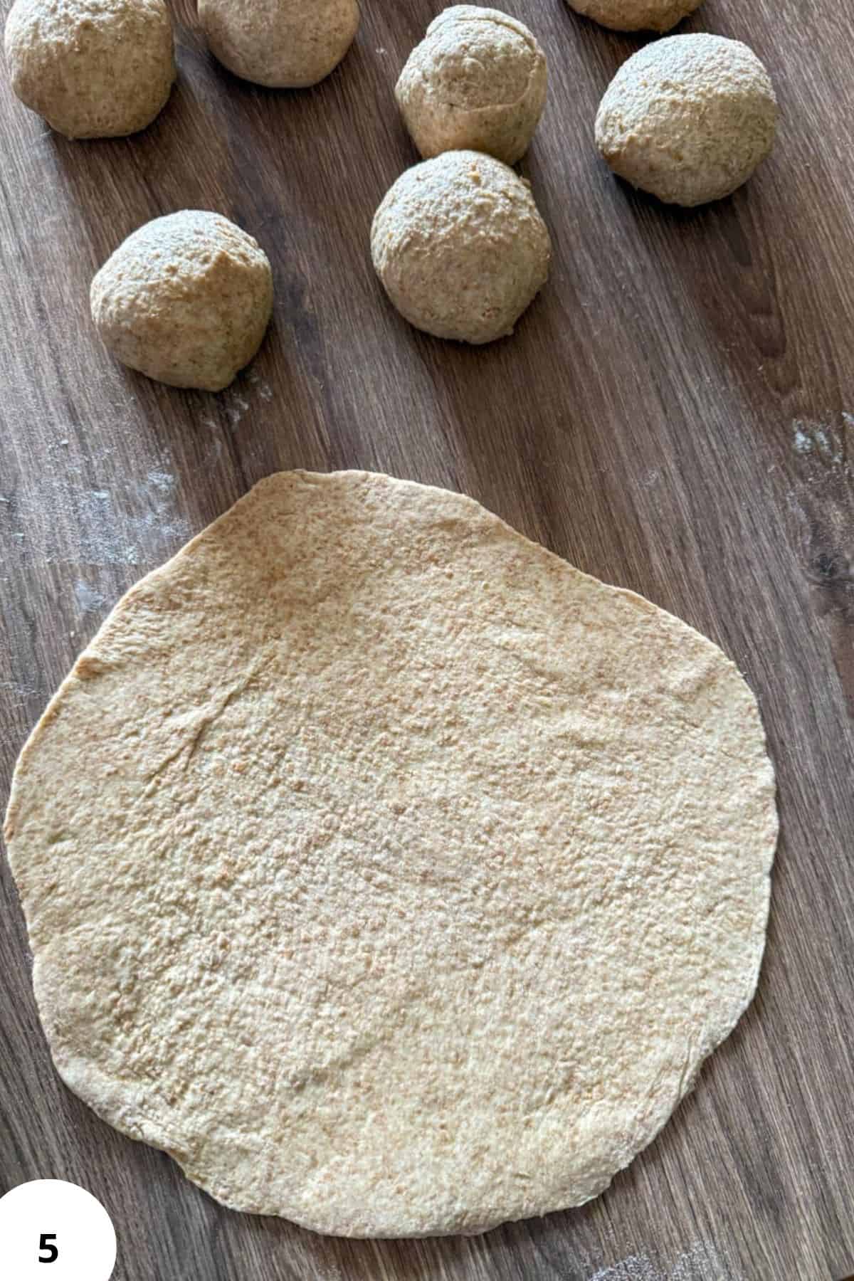 Freshly milled flour dough ball on wooden surface with smaller dough balls in background.
