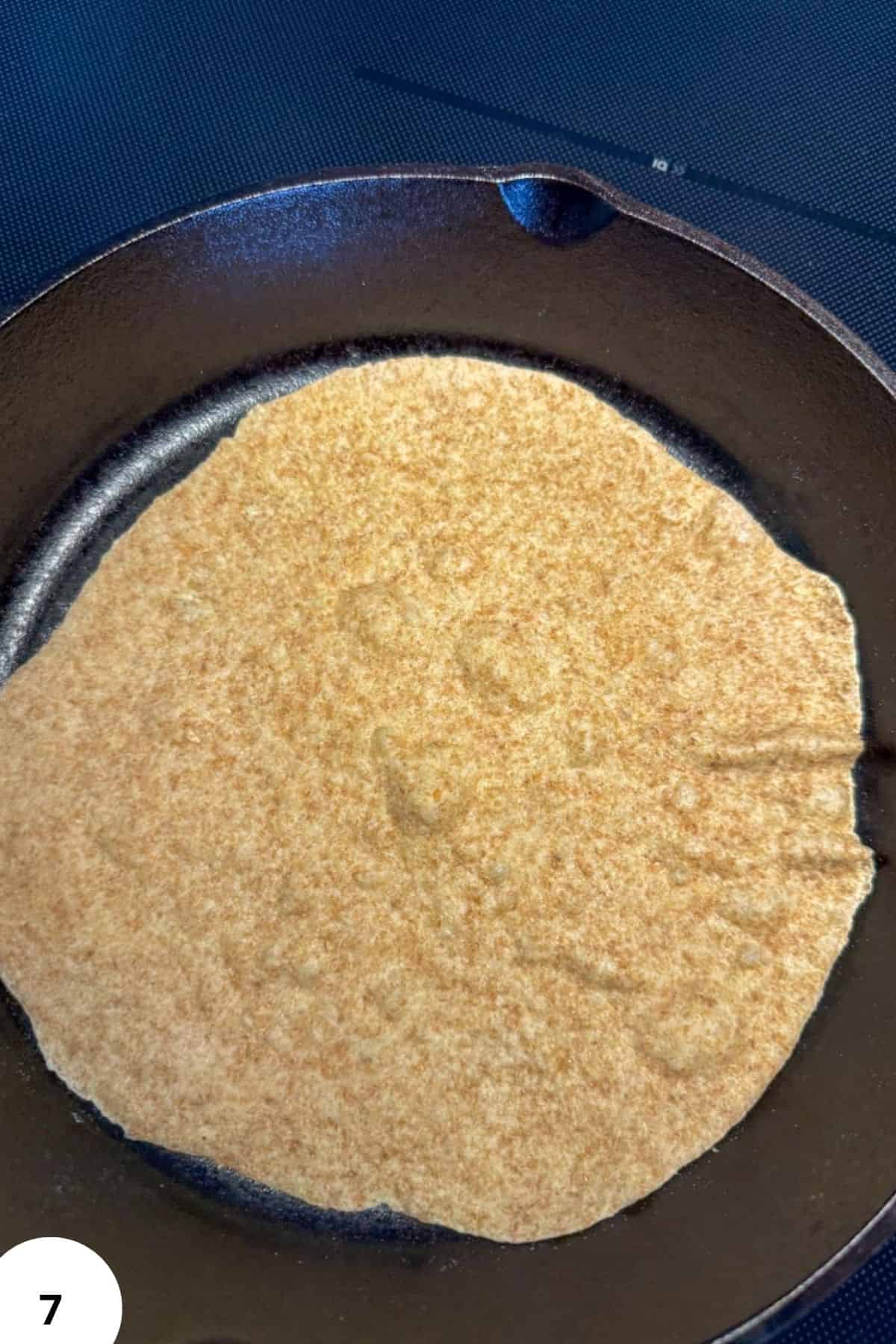 Freshly milled grain pancake cooking in a skillet, golden and crispy.