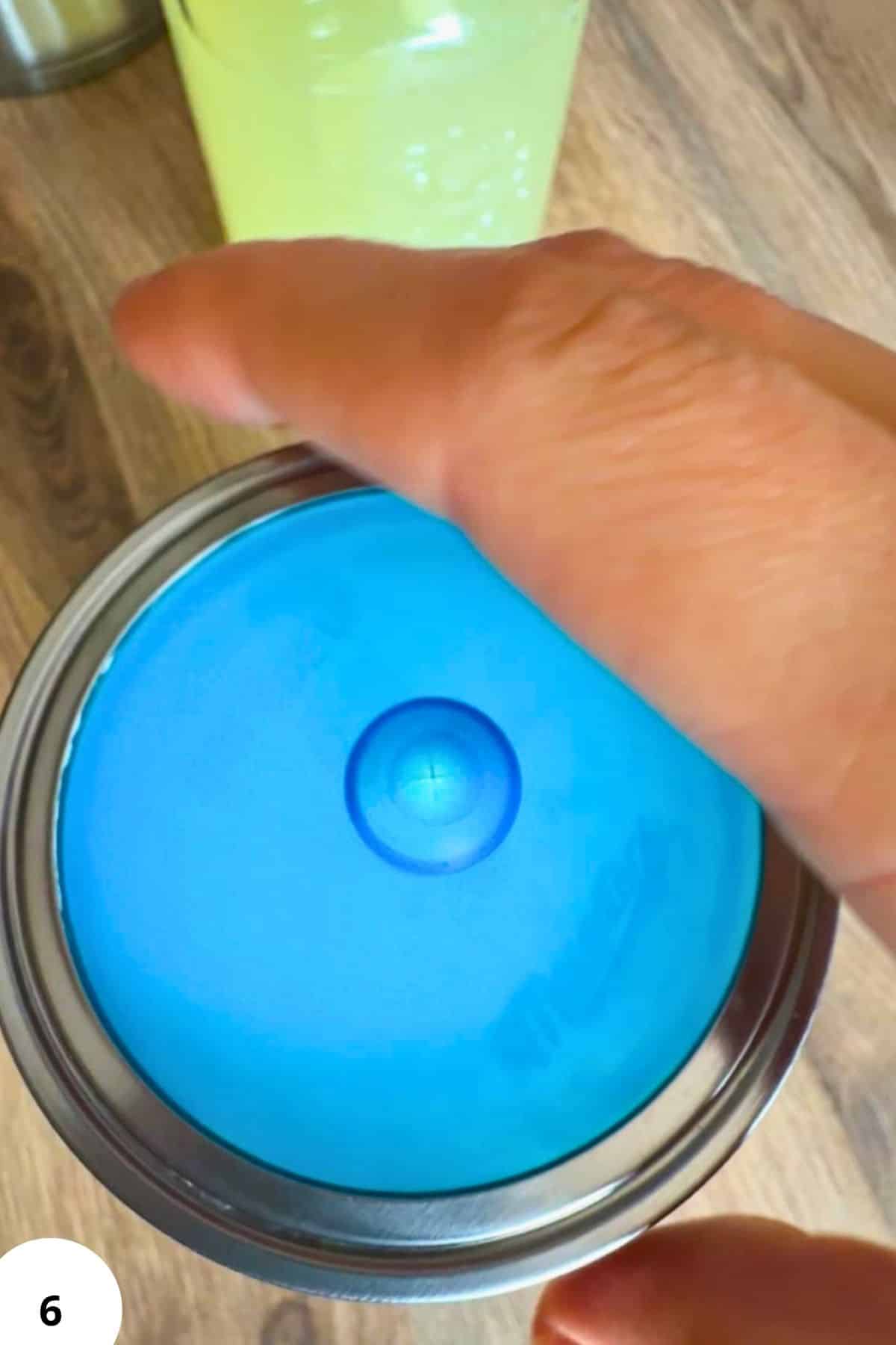 Hand performing stretch and fold technique on bread dough in a metal container.