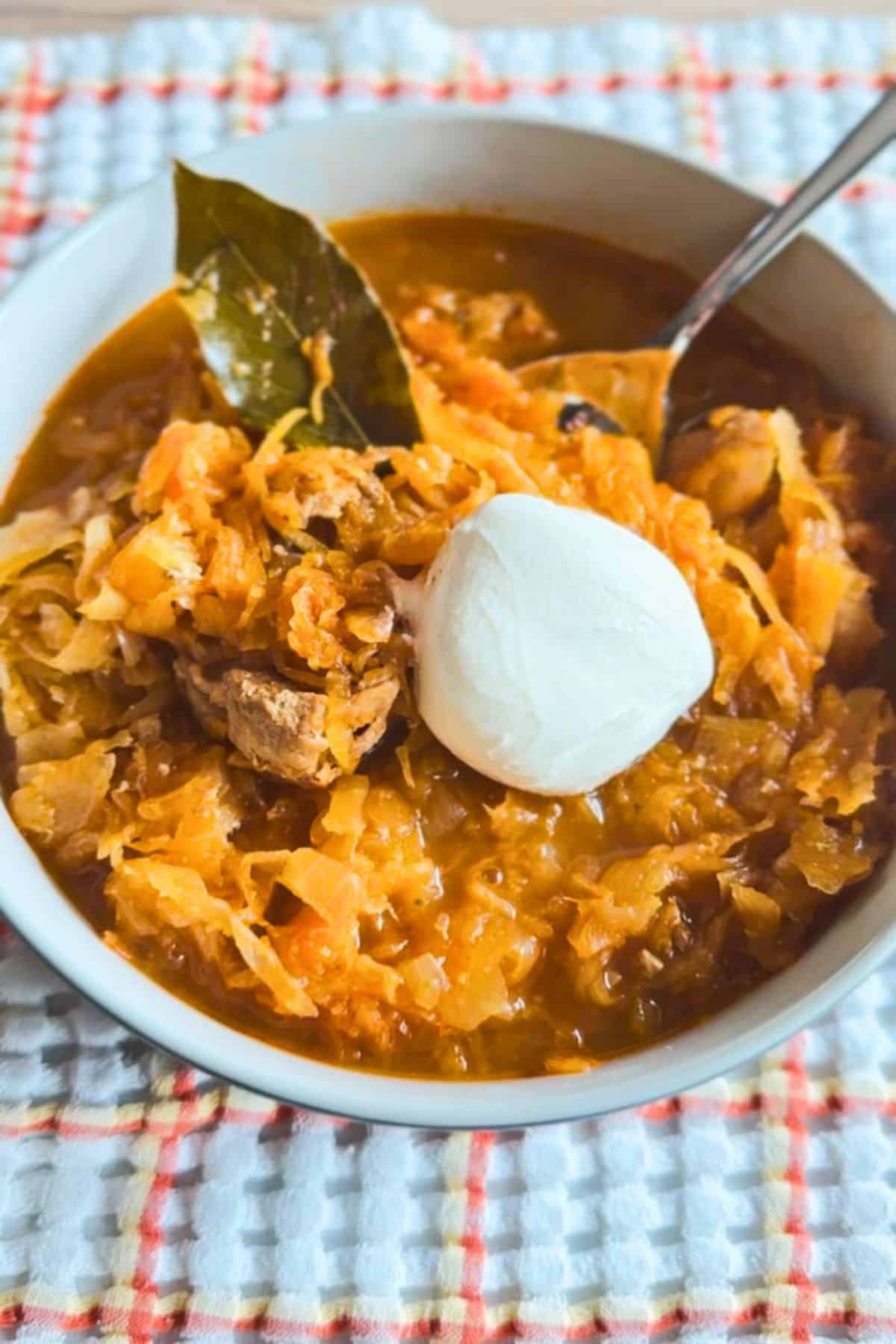 Pork and sauerkraut goulash served in a bowl with bay leaf and sour cream garnish.