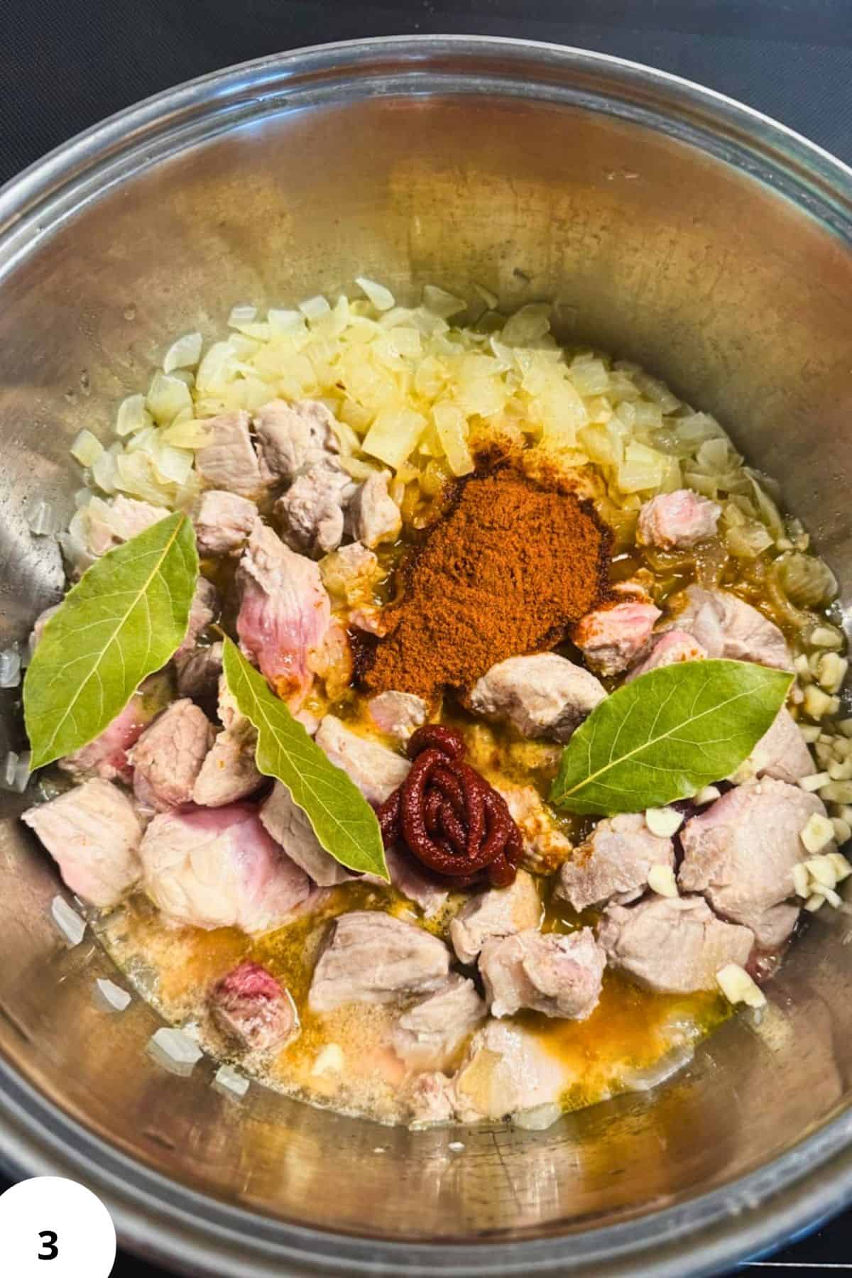 Pork and sauerkraut goulash ingredients with spices and bay leaves in a cooking pot.
