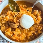 Hearty pork and sauerkraut goulash topped with sour cream in a white bowl.