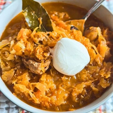 Hearty pork and sauerkraut goulash topped with sour cream in a white bowl.
