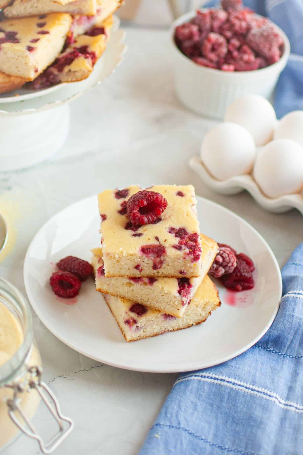 Delicious raspberry lemon bars with fresh berries on a white plate.