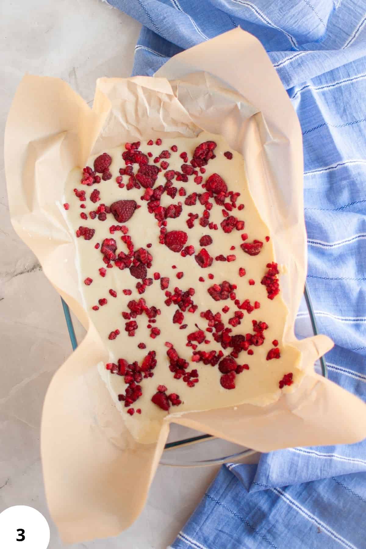 Delicious raspberry cheesecake in a baking dish with parchment paper, ready for baking or serving.
