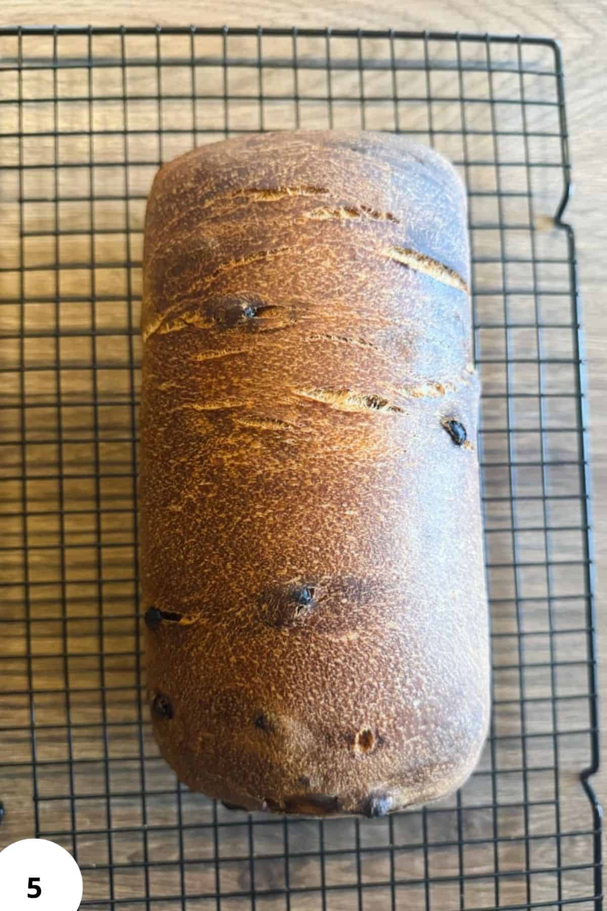 Sourdough bread loaf cooling on a wire rack, showcasing a rustic crust with dark spots.